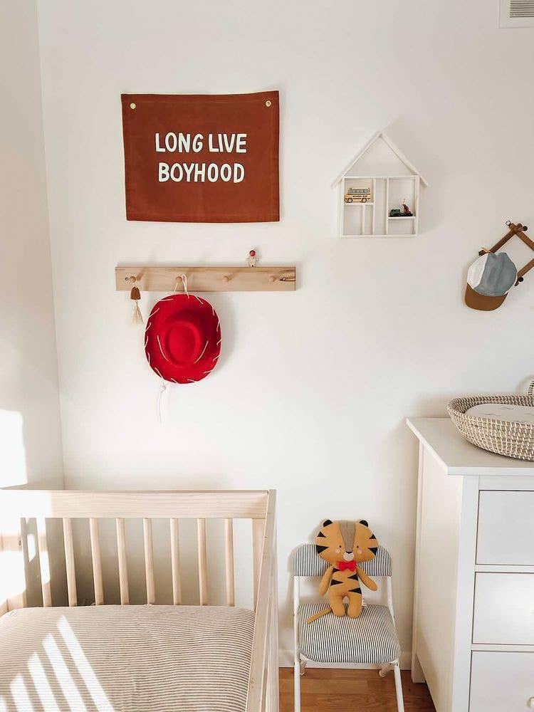 Minimalist nursery with crib, red hat, stuffed tiger, and 'Long Live Boyhood' sign. Come see us at Awaken, Franklin, Tennessee.