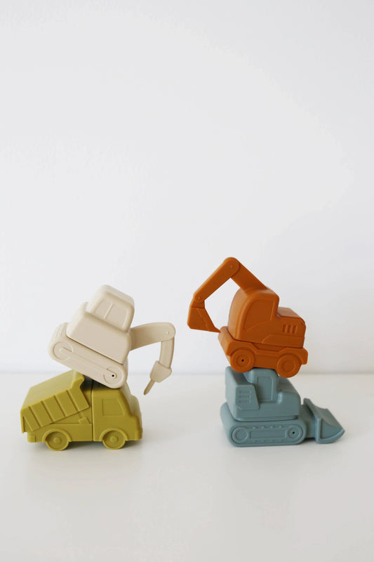 Stacked colorful toy construction vehicles on white surface with blank white background. Come see us at Awaken, Franklin, Tennessee