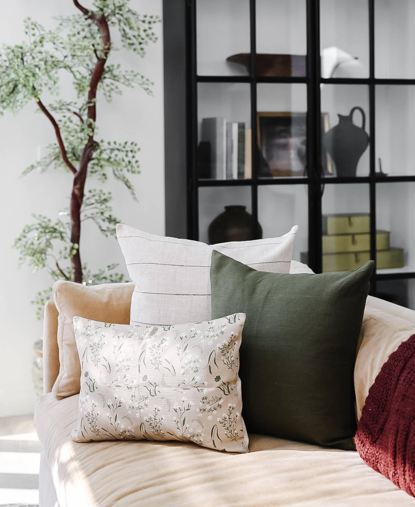 Beige sofa with three decorative pillows in green, white, and floral patterns, indoor plant and black shelf in background. Come see us at Awaken, Franklin, Tennessee