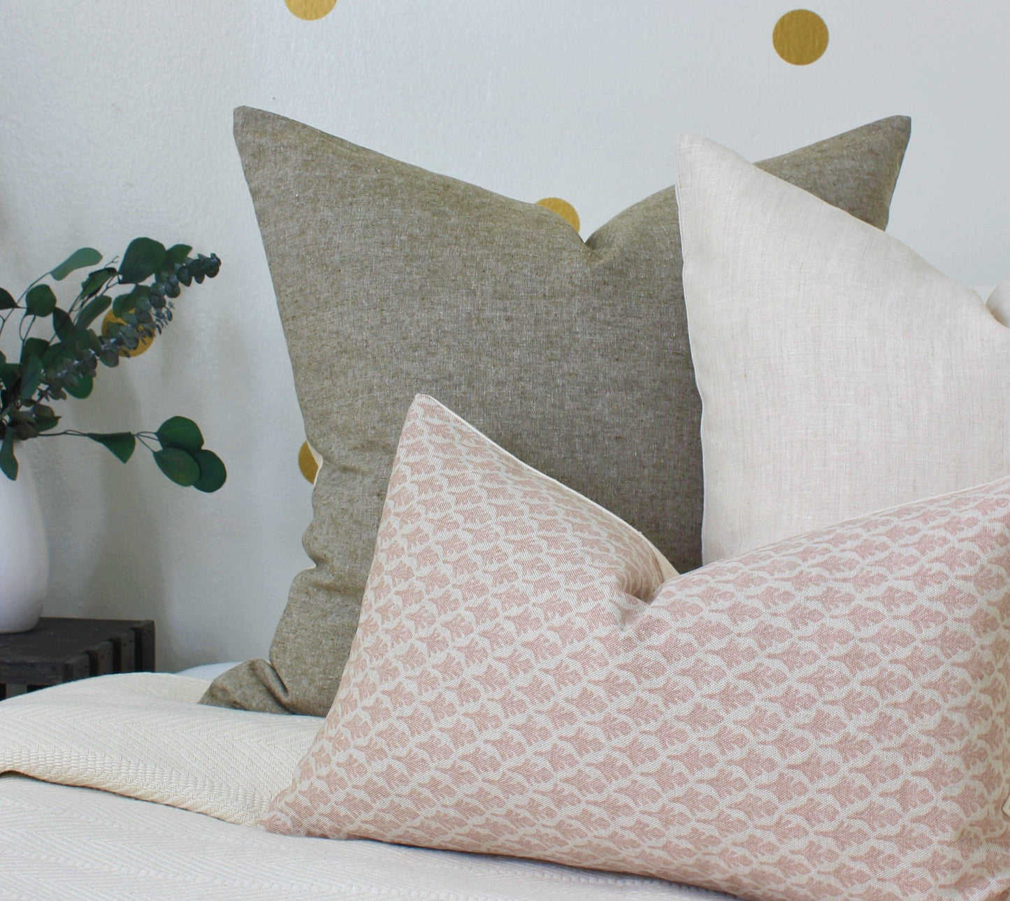 Decorative beige and gray pillows on white textured bed with eucalyptus plant, Come see us at Awaken, Franklin, Tennessee