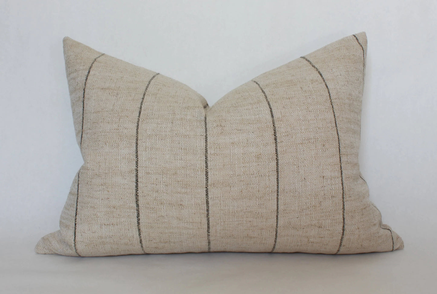 Neutral beige lumbar pillow with thin vertical black stripes on white background. Come see us at Awaken, Franklin, Tennessee