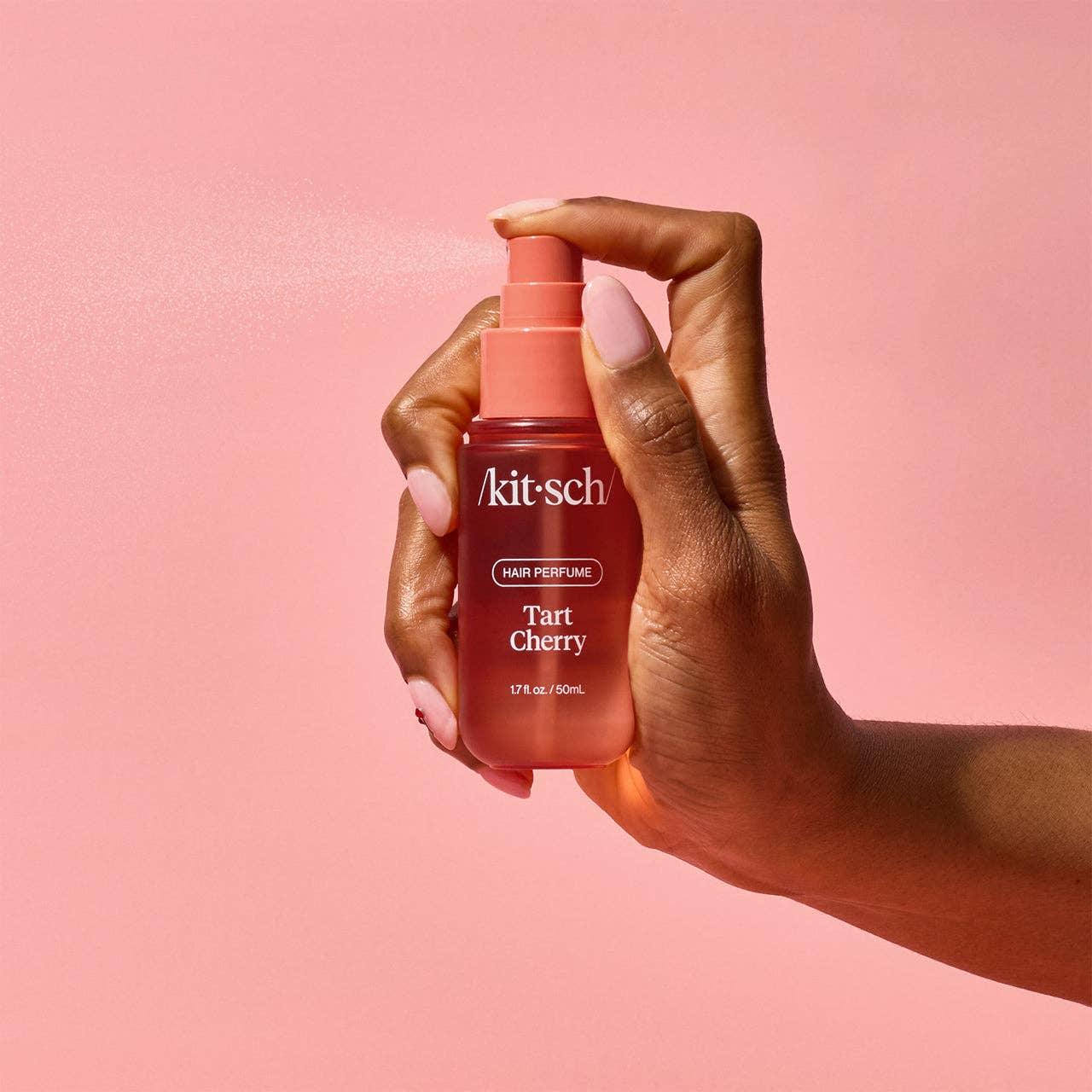 Hand spraying Kitsch Tart Cherry hair perfume against pink background, Come see us at Awaken, Franklin, Tennessee