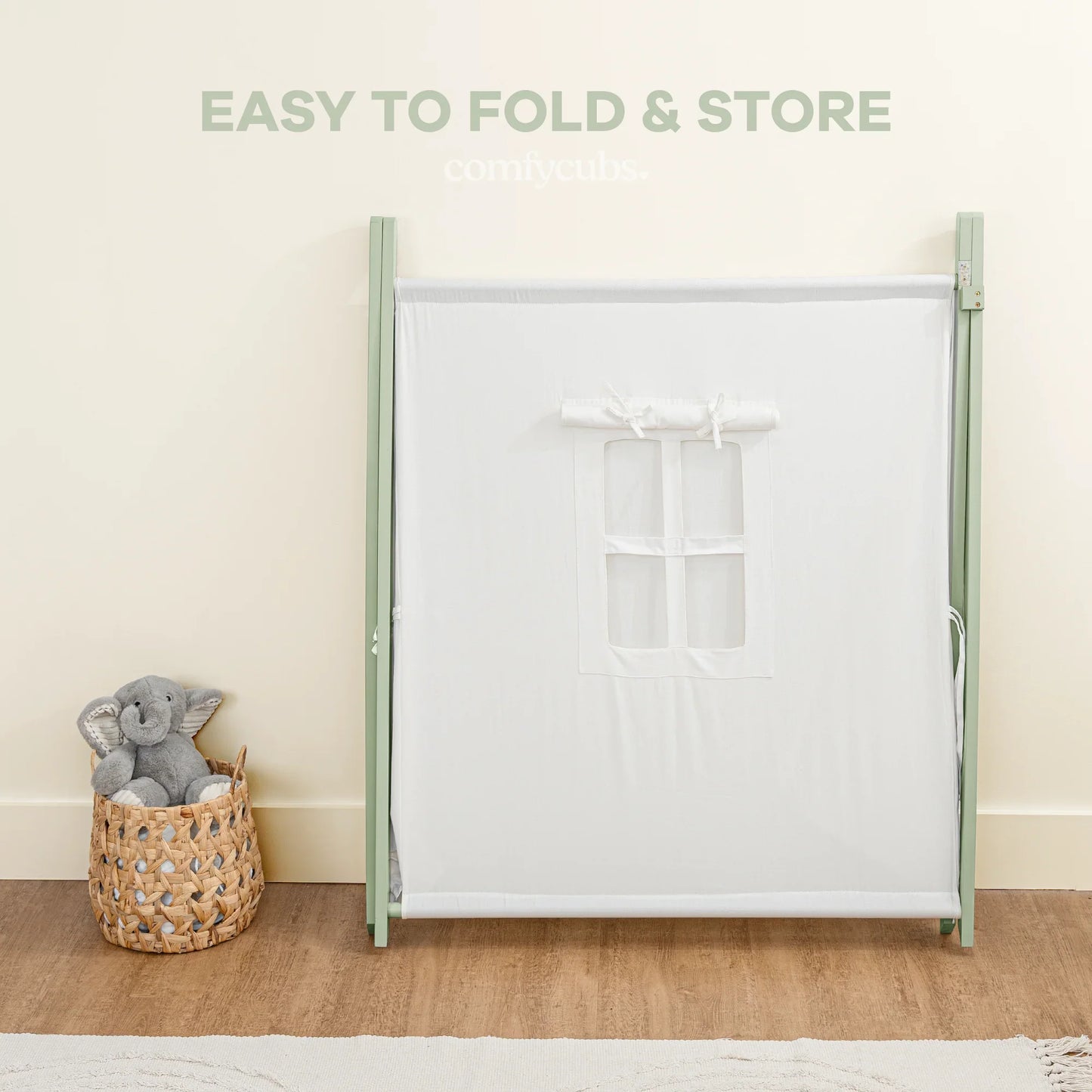 Foldable white baby playpen with small window, basket and stuffed elephant toy, wood floor. Come see us at Awaken, Franklin, Tennessee.