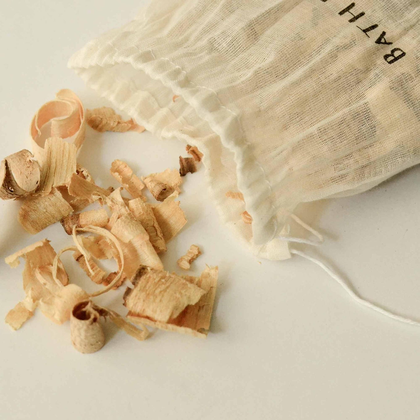 Wood shavings spilling from a white drawstring bag labeled BATH on white surface. Come see us at Awaken, Franklin, Tennessee