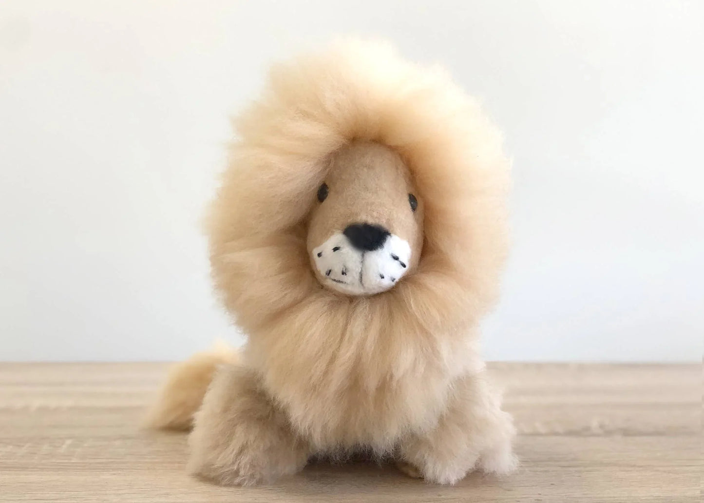 Fluffy handmade lion plush toy on wooden surface with white background. Come see us at Awaken, Franklin, Tennessee