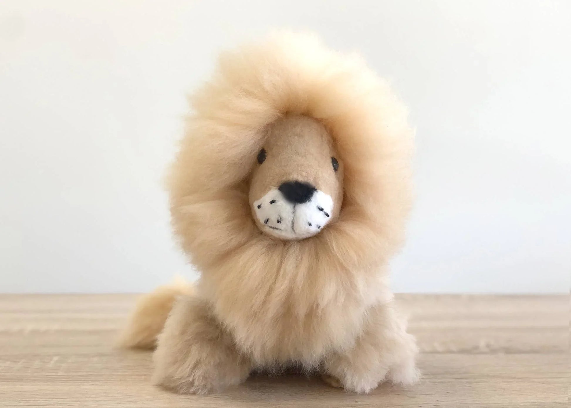 Fluffy handmade lion plush toy on wooden surface with white background. Come see us at Awaken, Franklin, Tennessee