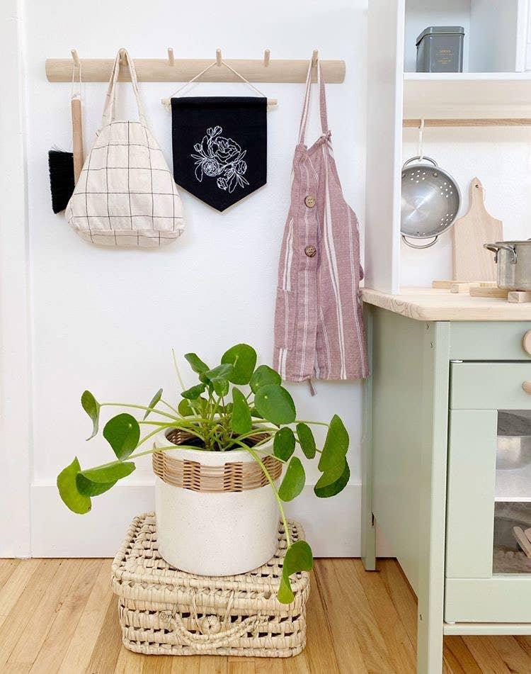 Modern kitchen decor with a hanging apron, tote bag, black floral flag, and potted plant. Come see us at Awaken, Franklin, Tennessee.