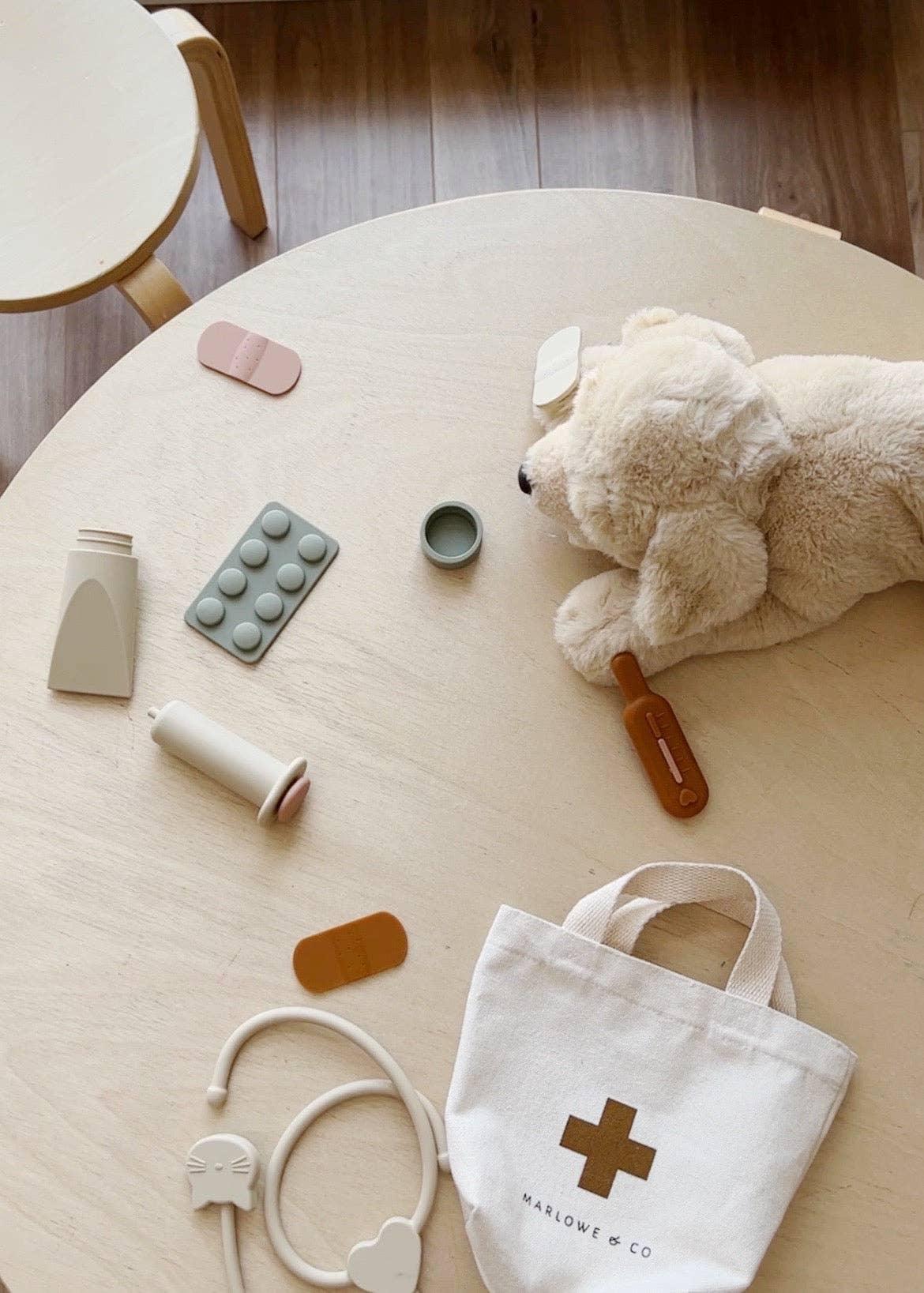Kids' doctor play set with stuffed dog, toy medicine, and bag on wooden table. Come see us at Awaken, Franklin, Tennessee.