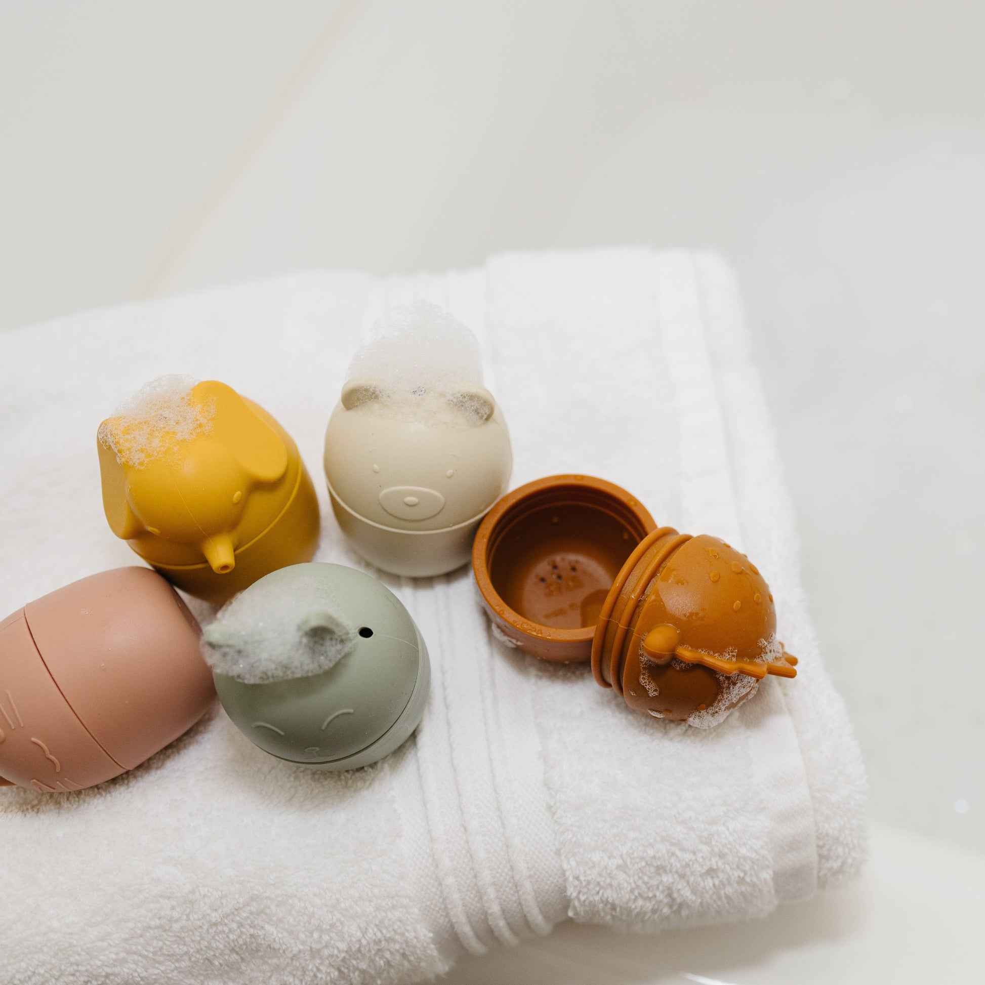 Silicone animal-shaped bath toys with foam on white towel in bathroom. Come see us at Awaken, Franklin, Tennessee