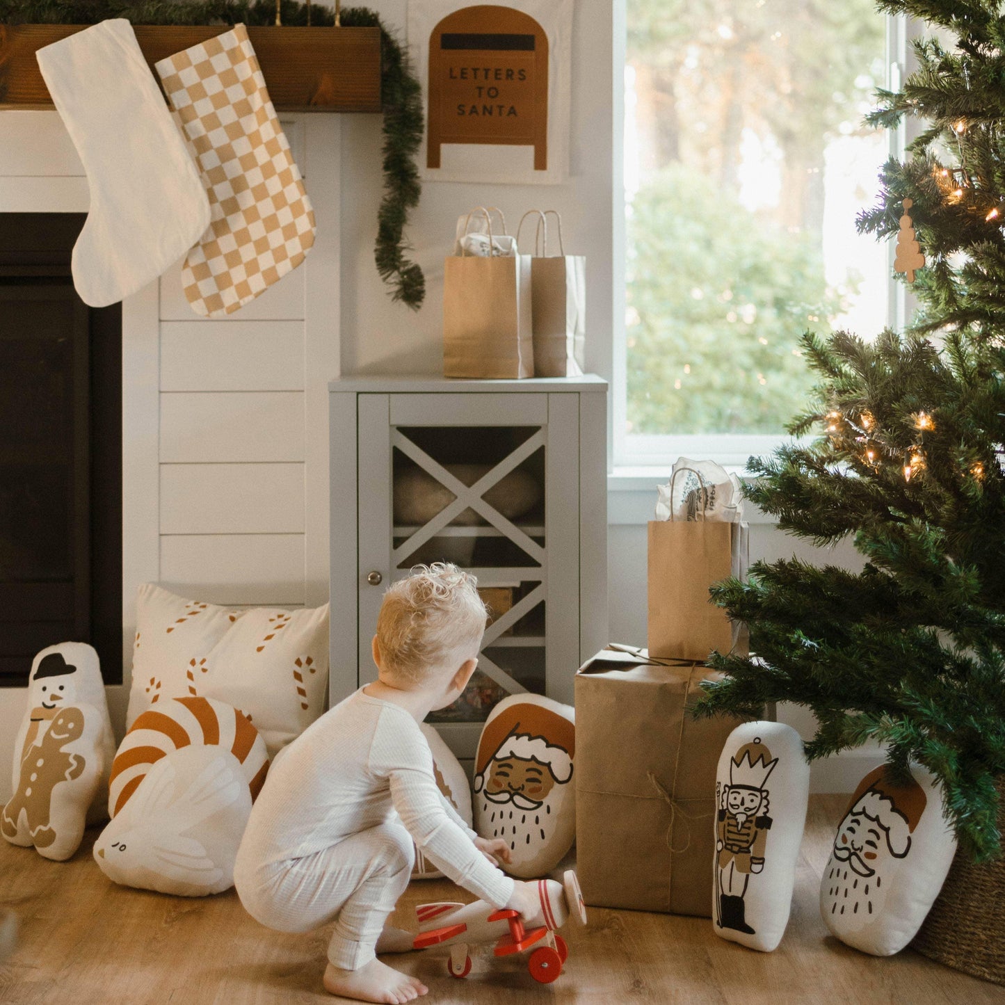 Toddler playing near decorated Christmas tree, festive pillows, stockings, and presents. Come see us at Awaken, Franklin, Tennessee.