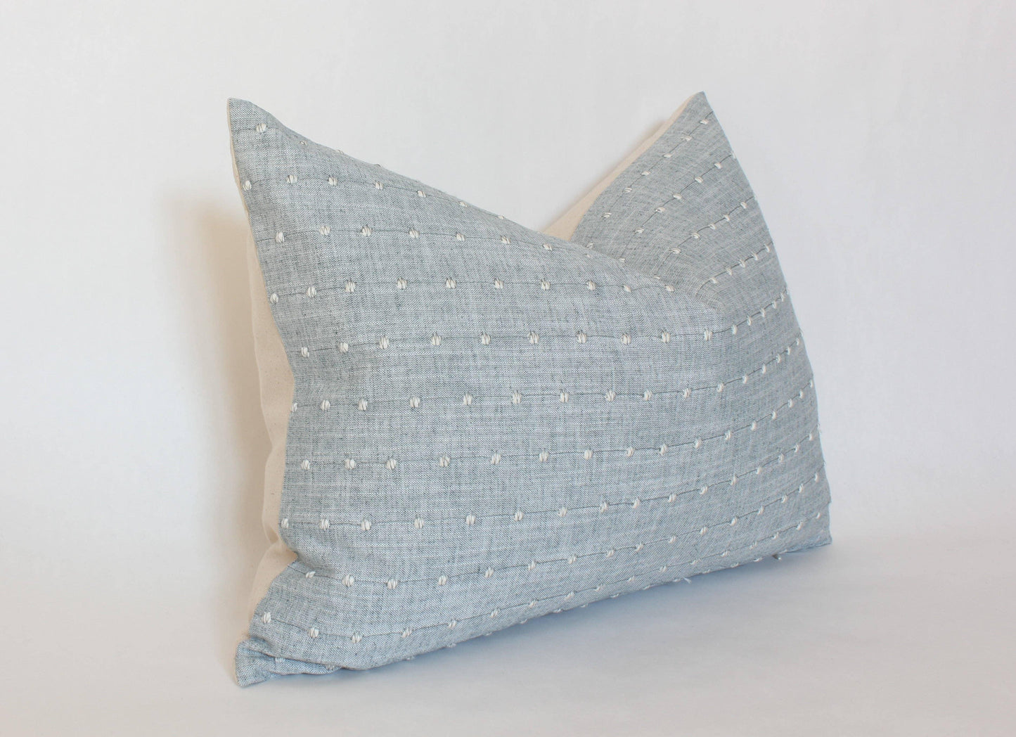 Gray decorative pillow with white stitch dots on beige backing, studio setting; Come see us at Awaken, Franklin, Tennessee