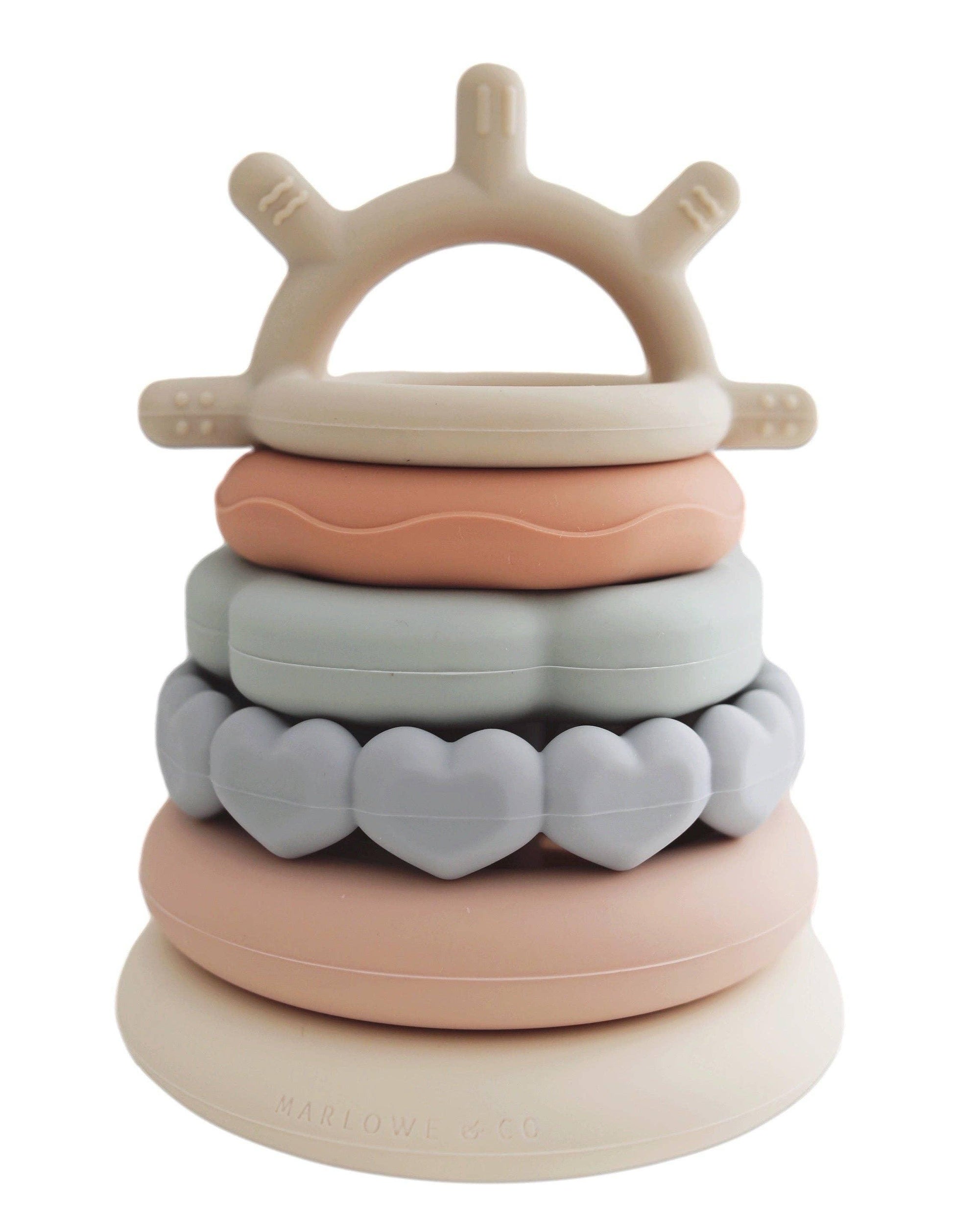 Silicone baby stacking toy with heart, ring, and wave shapes in soft pastels, Come see us at Awaken, Franklin, Tennessee