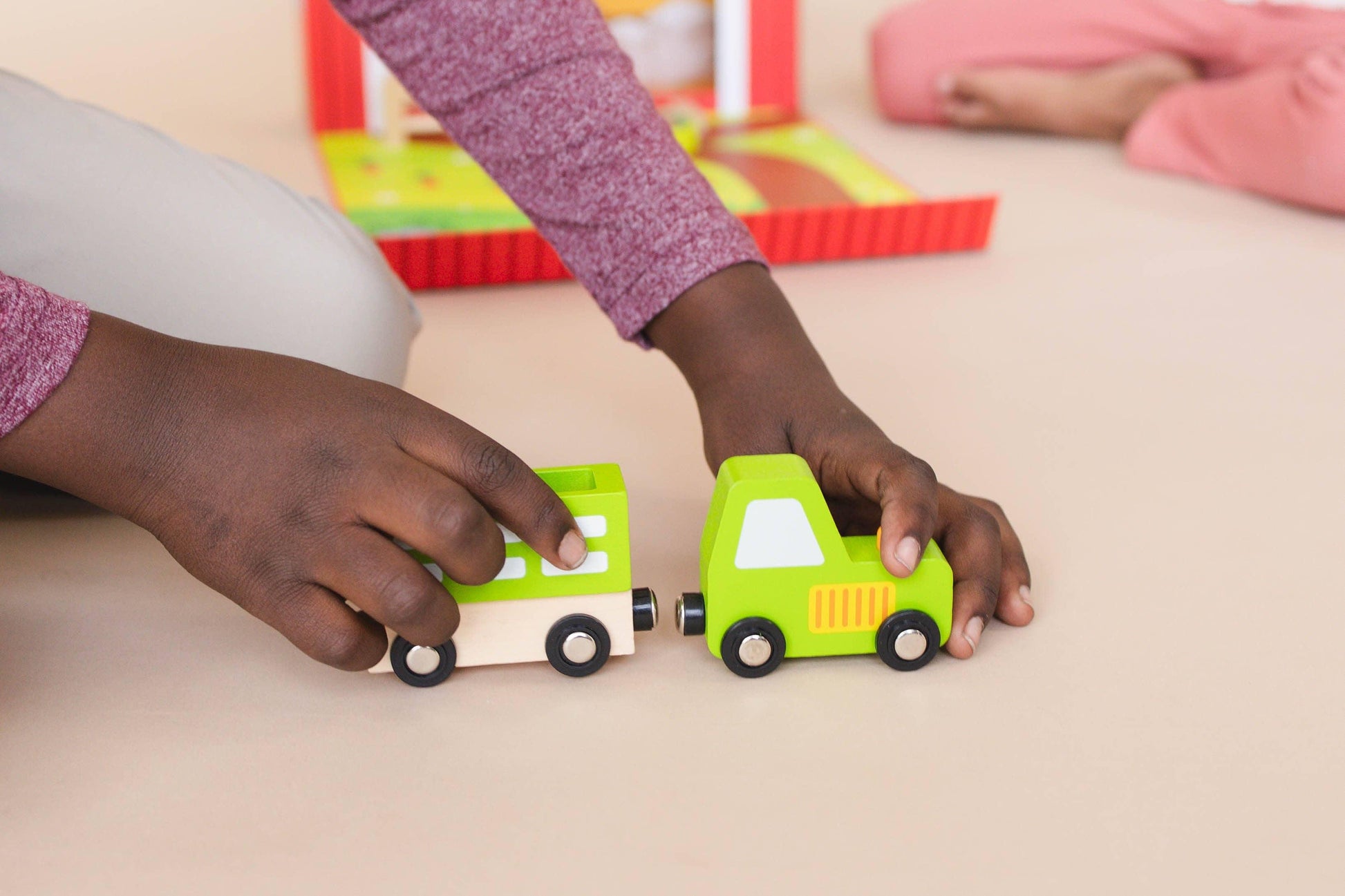 Child playing with green wooden toy cars on beige floor. Come see us at Awaken, Franklin, Tennessee
