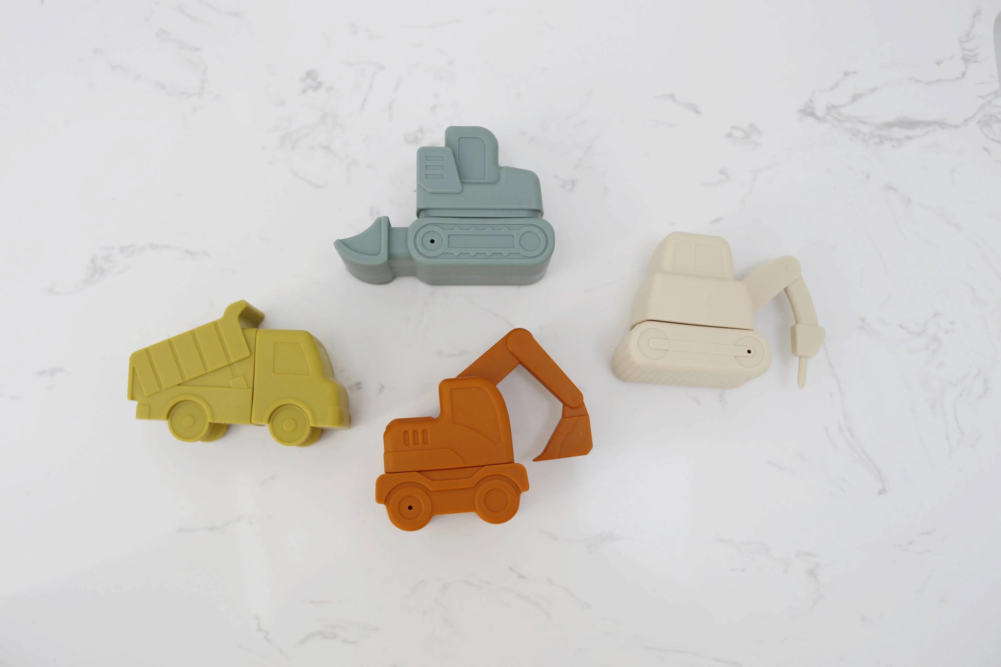 Four colorful silicone construction vehicle toys on white marble background. Come see us at Awaken, Franklin, Tennessee