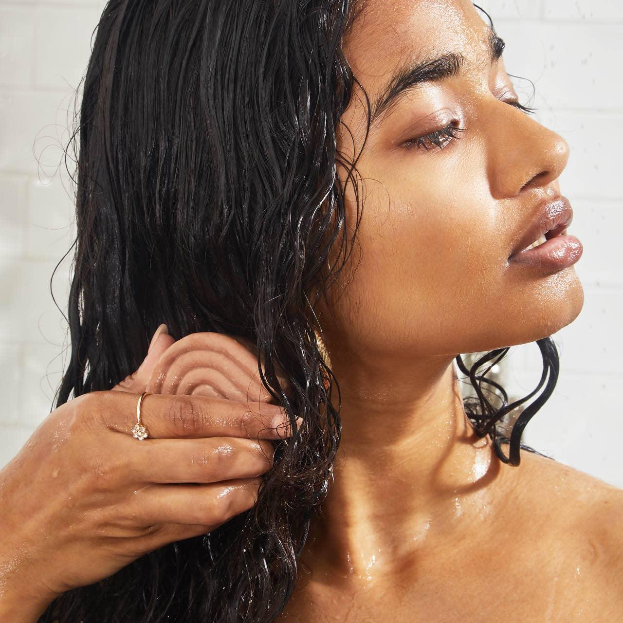 Woman using scalp massager on wet hair in shower, Come see us at Awaken, Franklin, Tennessee