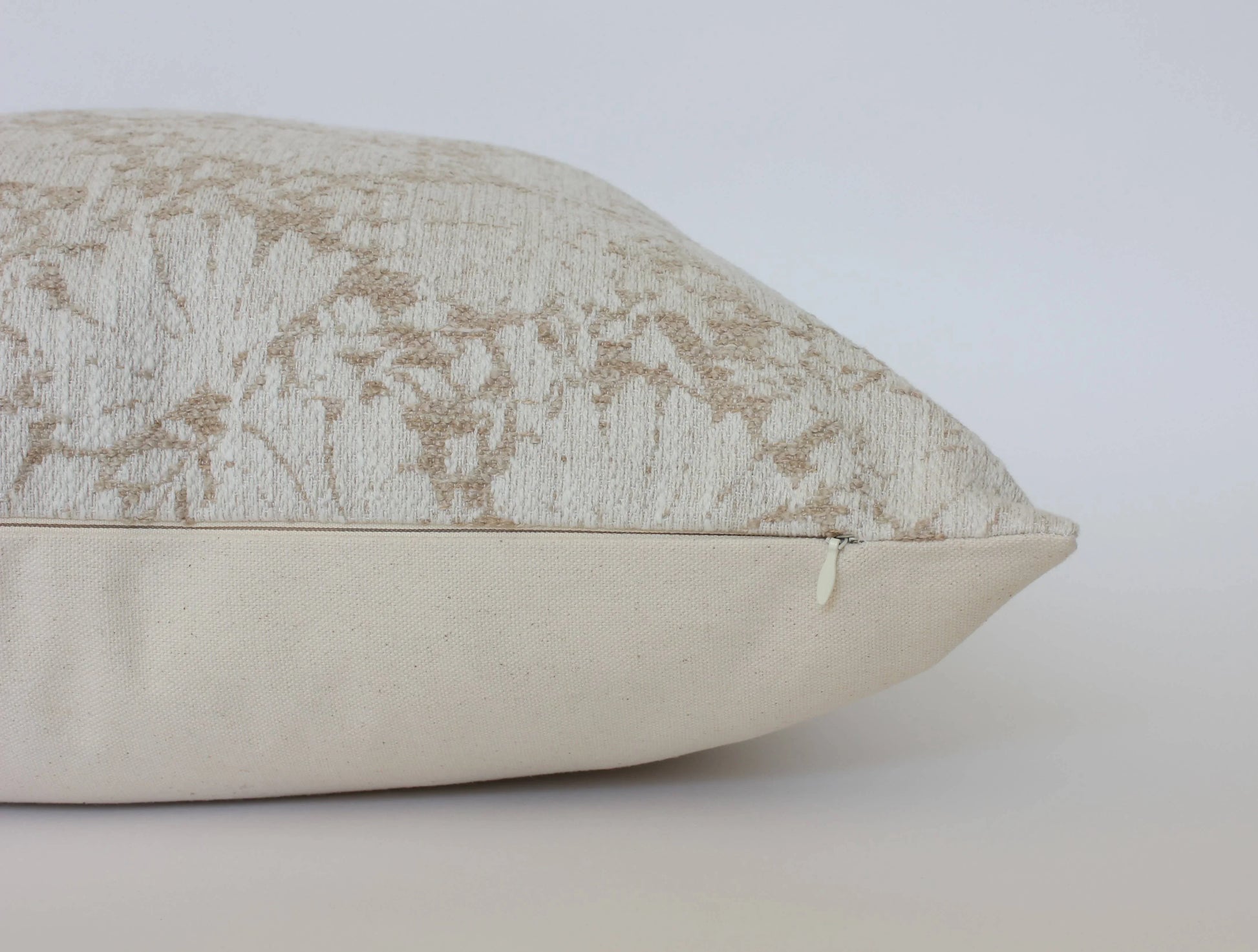 Side view of beige and cream textured decorative pillow with zipper detail, plain background. Come see us at Awaken, Franklin, Tennessee