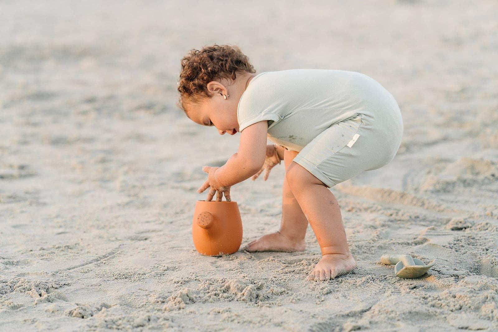 Toddler playing with sand toy on beach, barefoot in light outfit. Come see us at Awaken, Franklin, Tennessee
