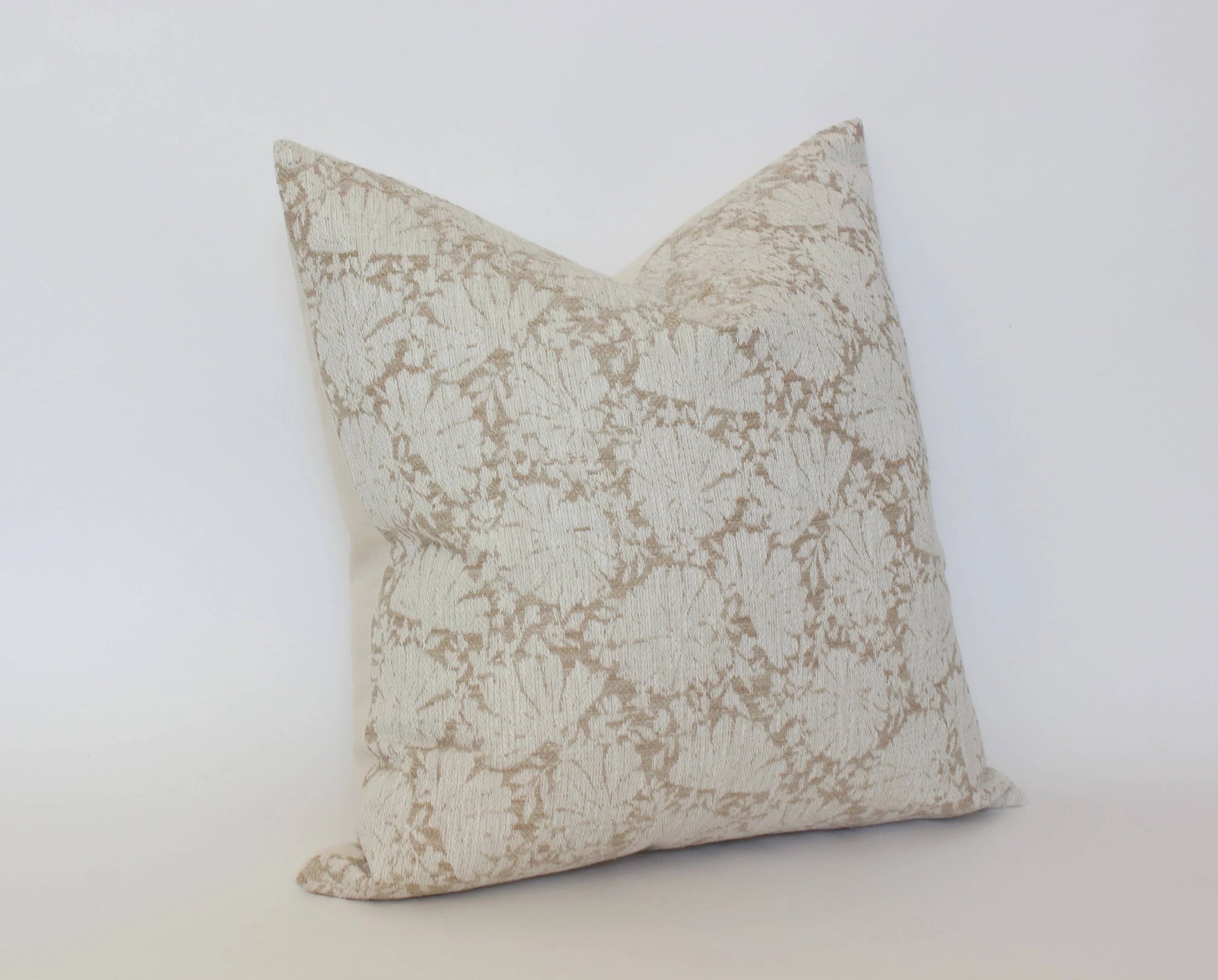 Beige decorative pillow with subtle floral pattern on white background. Come see us at Awaken, Franklin, Tennessee