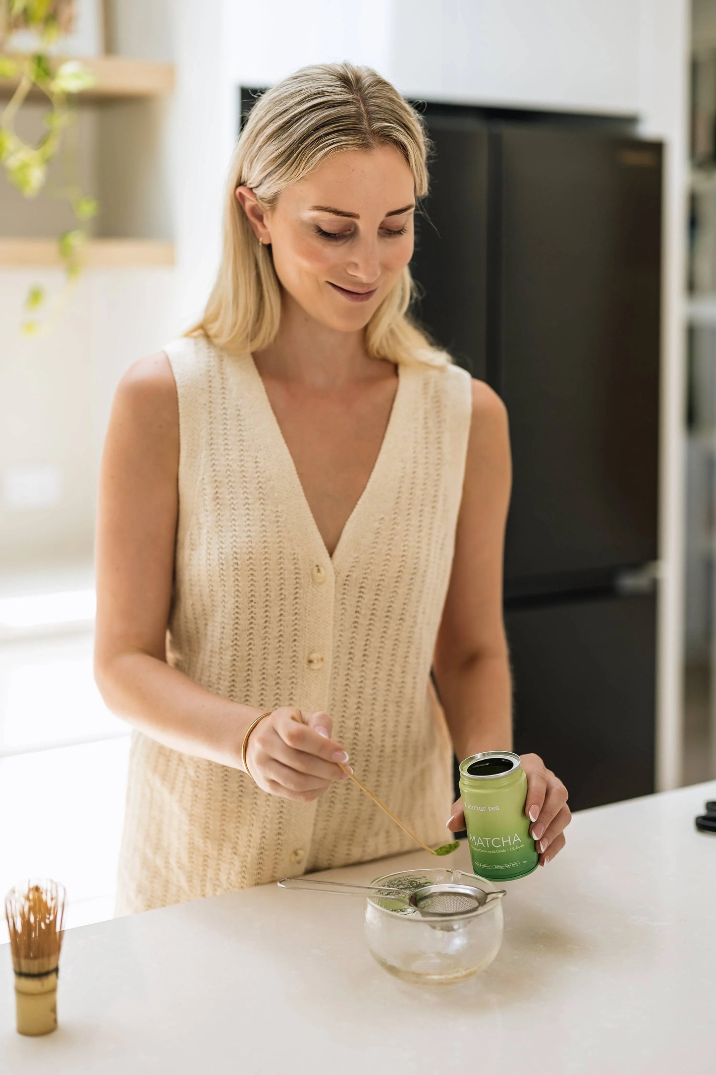 Woman in beige sleeveless top preparing matcha tea in kitchen. Come see us at Awaken, Franklin, Tennessee