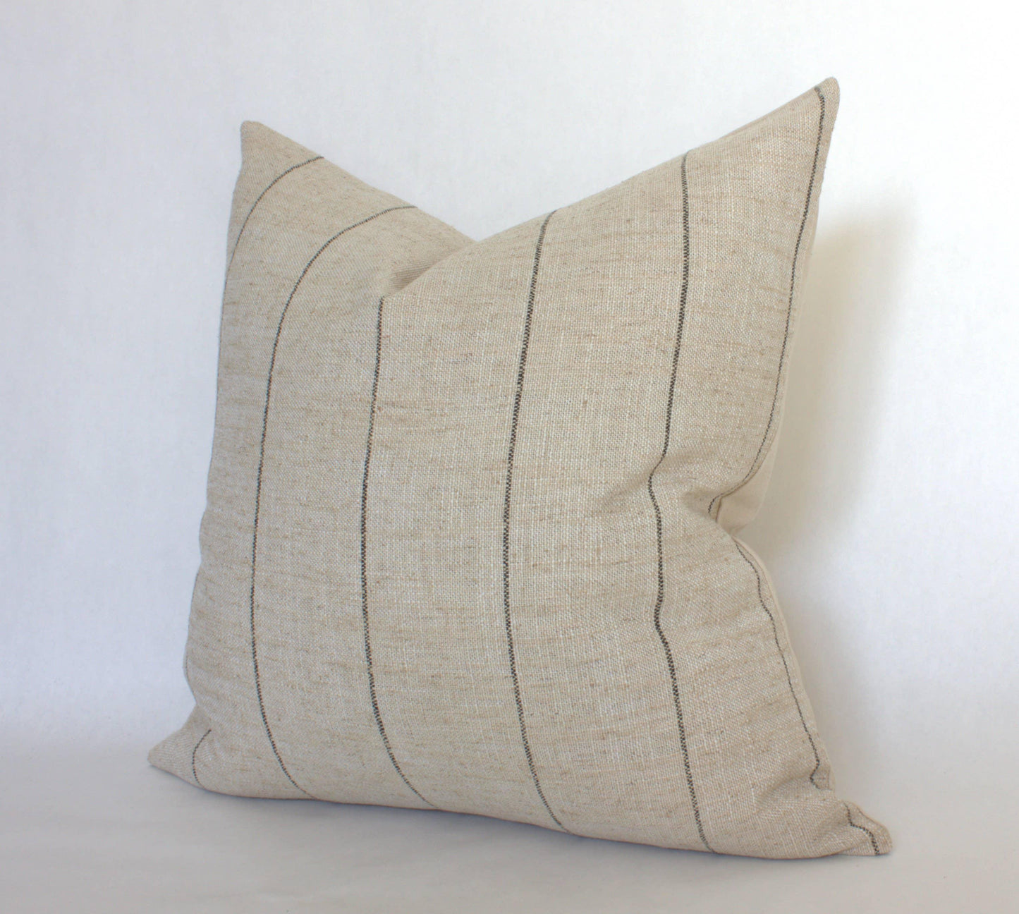 Beige linen pillow with thin black vertical stripes on white background. Come see us at Awaken, Franklin, Tennessee