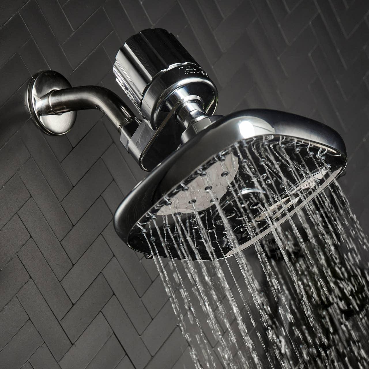 Modern chrome shower head spraying water, dark tile background. Come see us at Awaken, Franklin, Tennessee