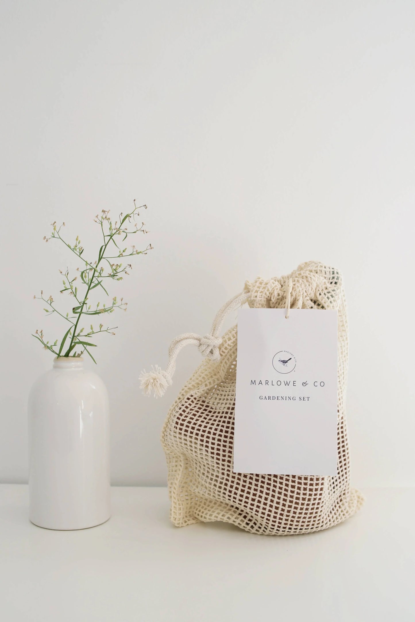 Marlowe & Co gardening set in mesh bag next to white ceramic vase with green twig, Come see us at Awaken, Franklin, Tennessee