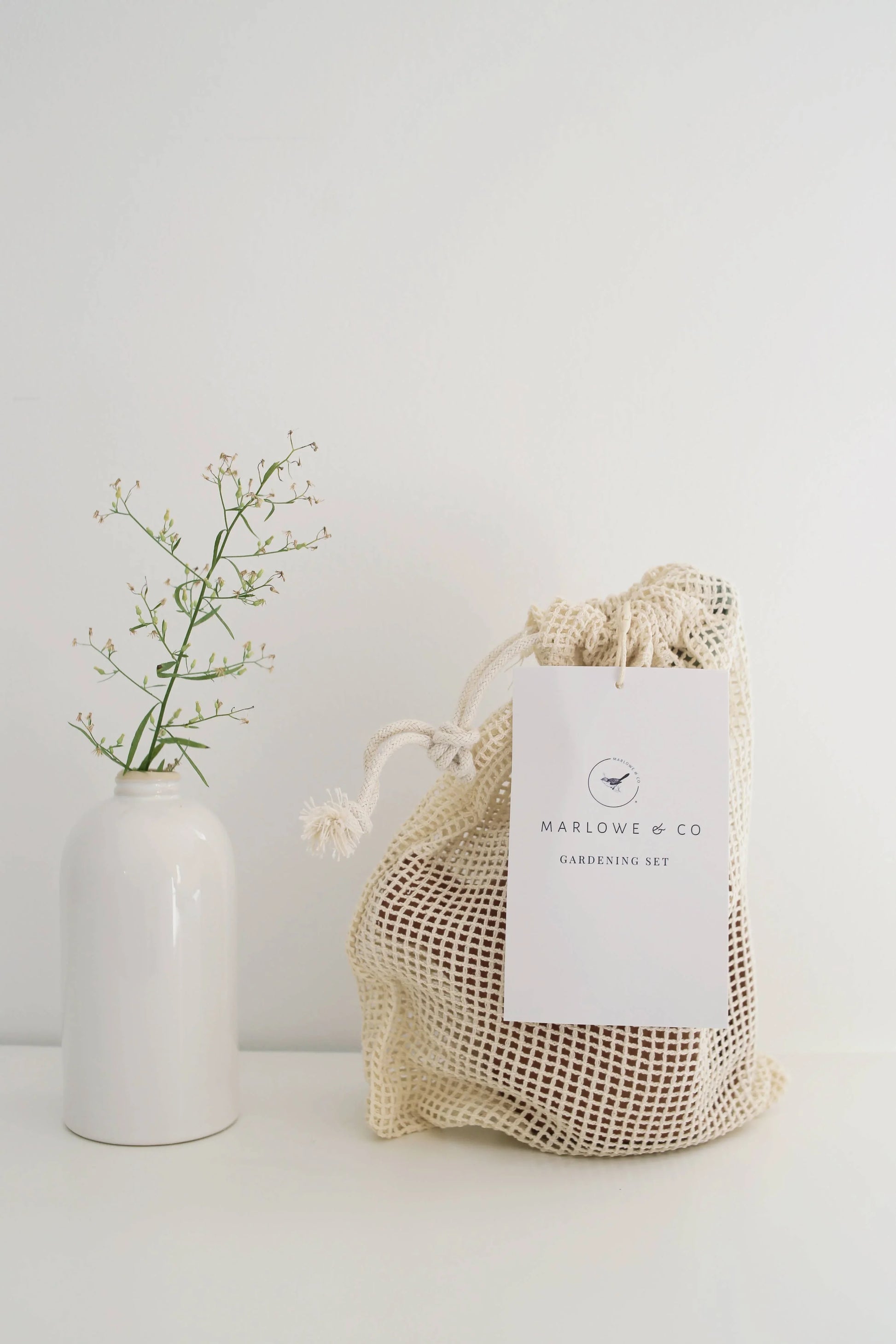 Marlowe & Co gardening set in mesh bag next to white ceramic vase with green twig, Come see us at Awaken, Franklin, Tennessee