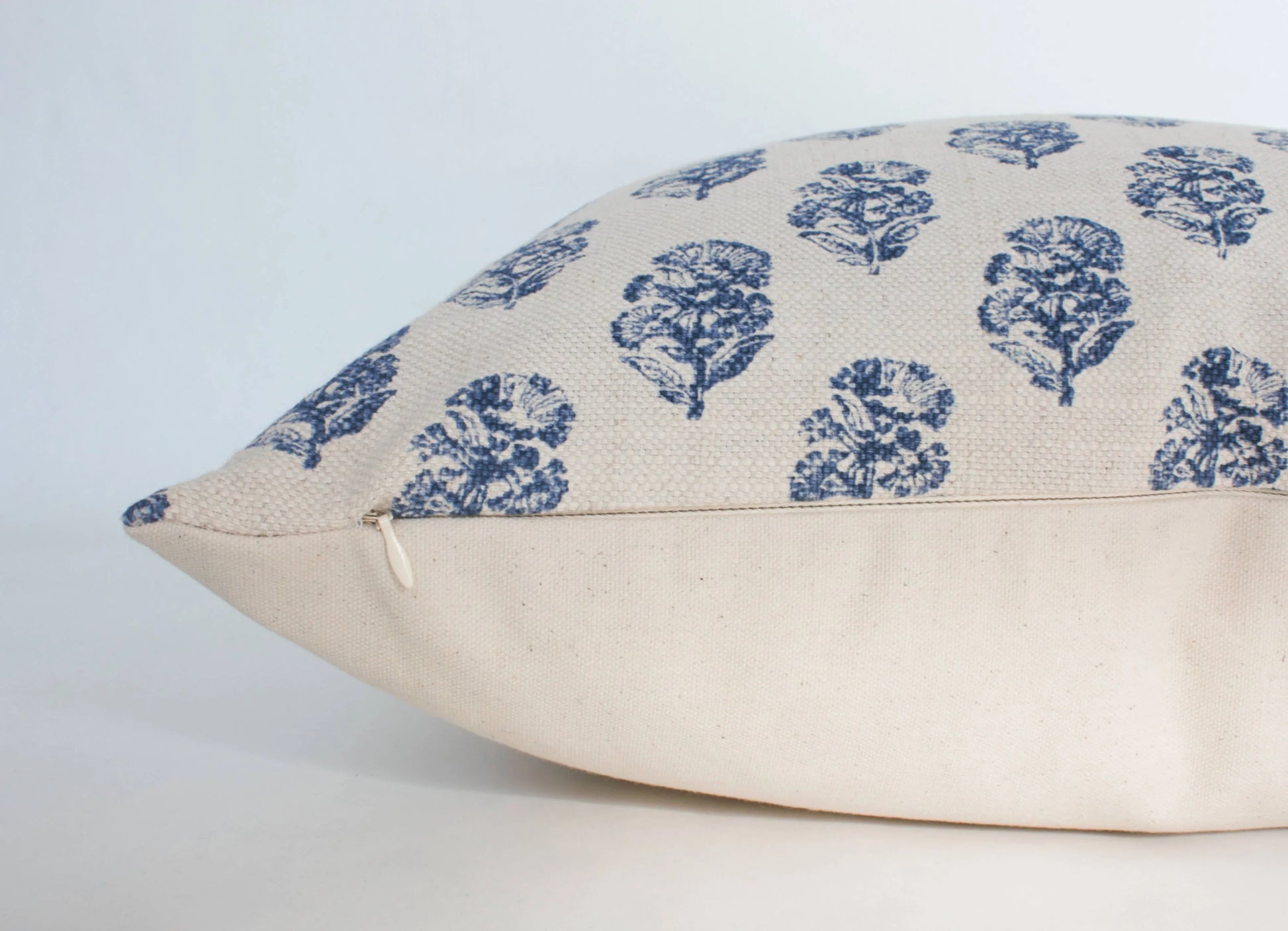 Beige linen pillow with blue floral prints and zipper detail on white background. Come see us at Awaken, Franklin, Tennessee