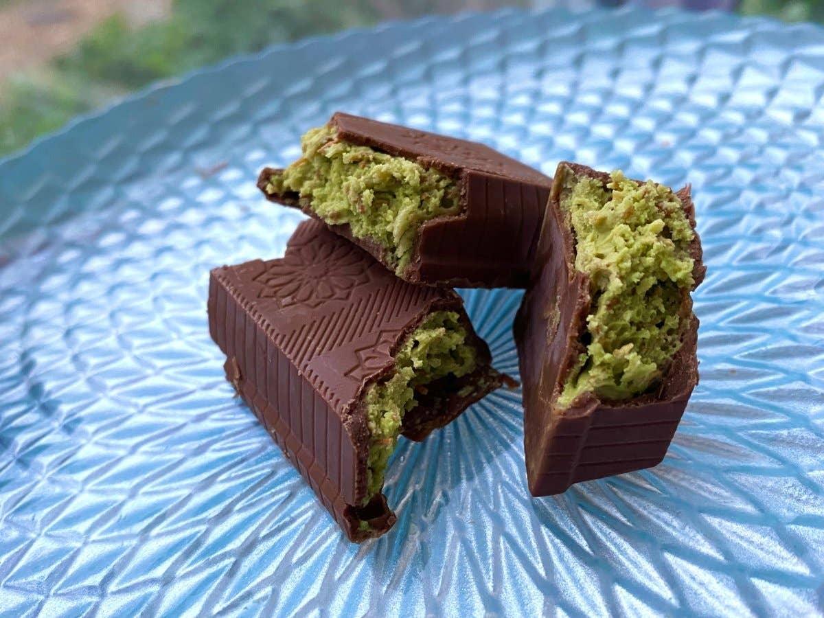 Three pieces of dark chocolate with green matcha filling on a textured blue plate. Come see us at Awaken, Franklin, Tennessee