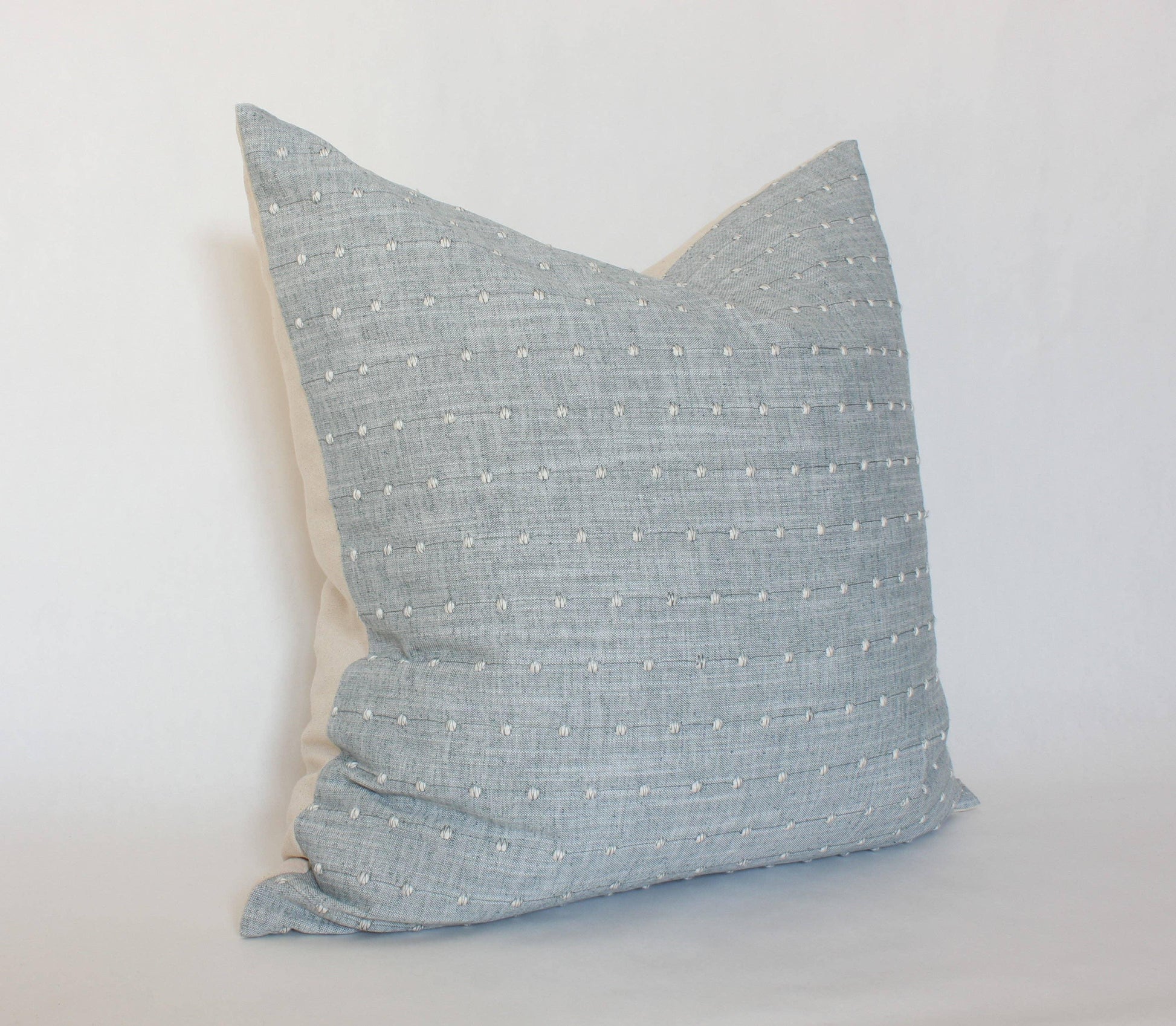 Soft blue decorative pillow with white textured dots on neutral background. Come see us at Awaken, Franklin, Tennessee