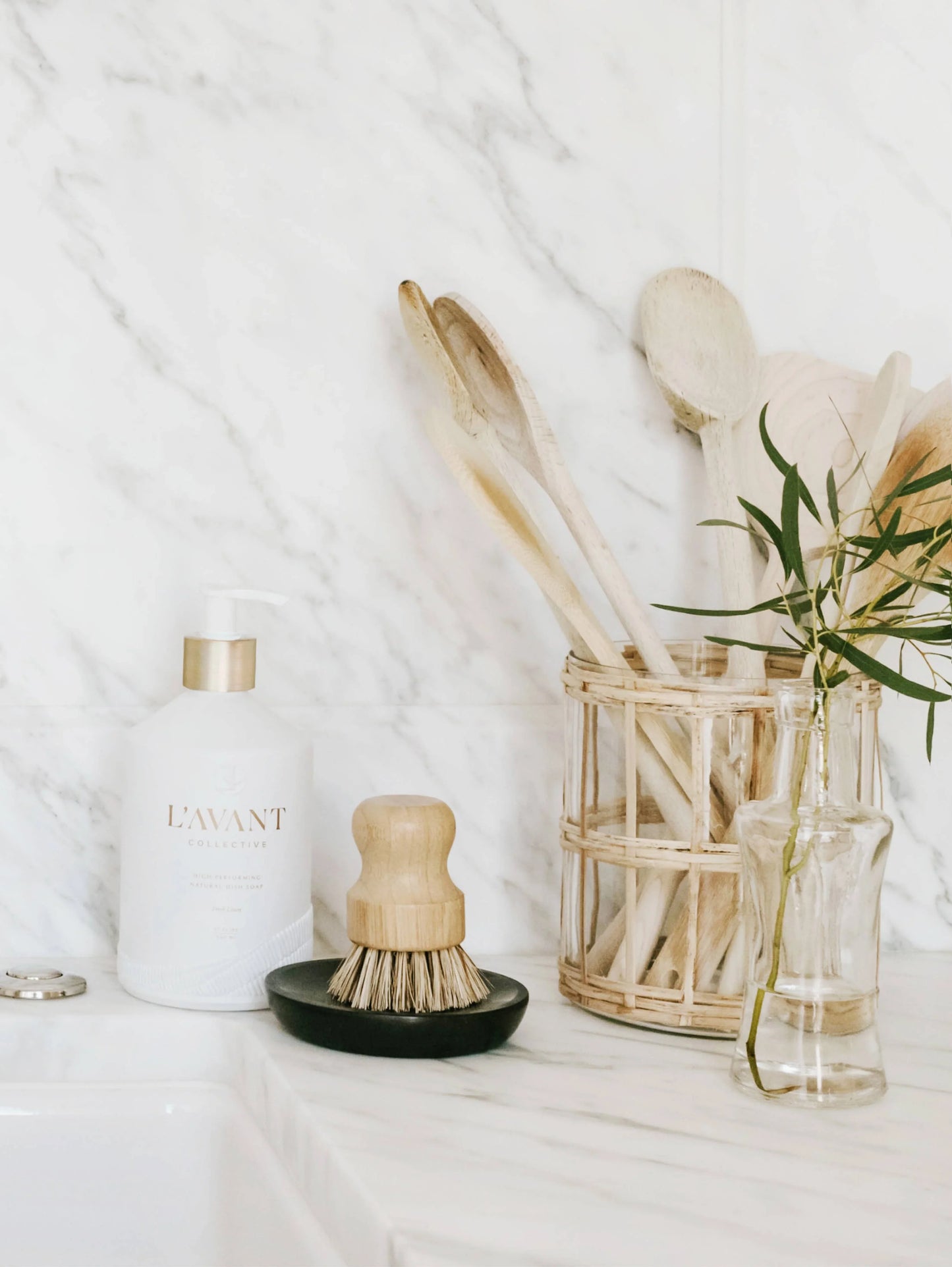 Minimalist kitchen scene with L'AVANT soap, wooden utensils, and glass vase on marble. Come see us at Awaken, Franklin, Tennessee