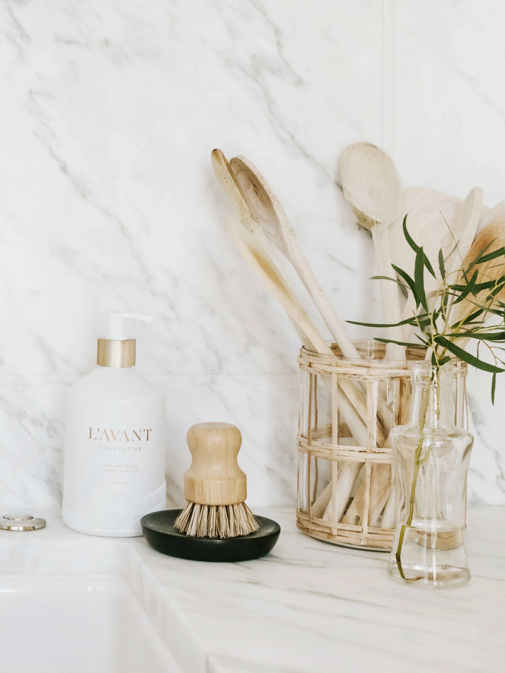 Minimalist kitchen scene with L'AVANT soap, wooden utensils, and glass vase on marble. Come see us at Awaken, Franklin, Tennessee