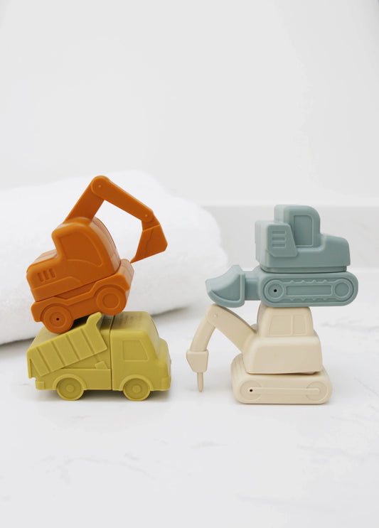 Stacked pastel toy construction vehicles on white surface with towel, Come see us at Awaken, Franklin, Tennessee