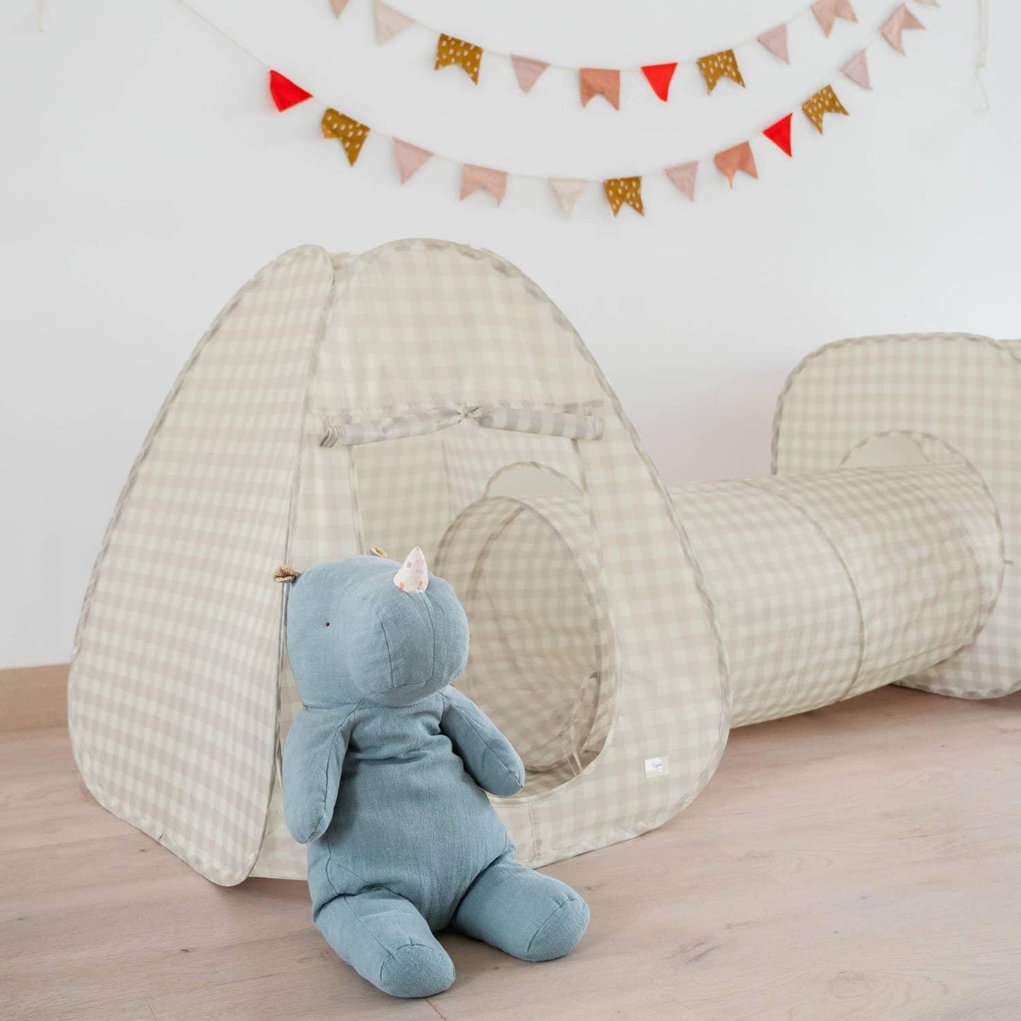 Blue stuffed rhino toy sitting beside beige checkered kids play tent with tunnel in light room. Come see us at Awaken, Franklin, Tennessee