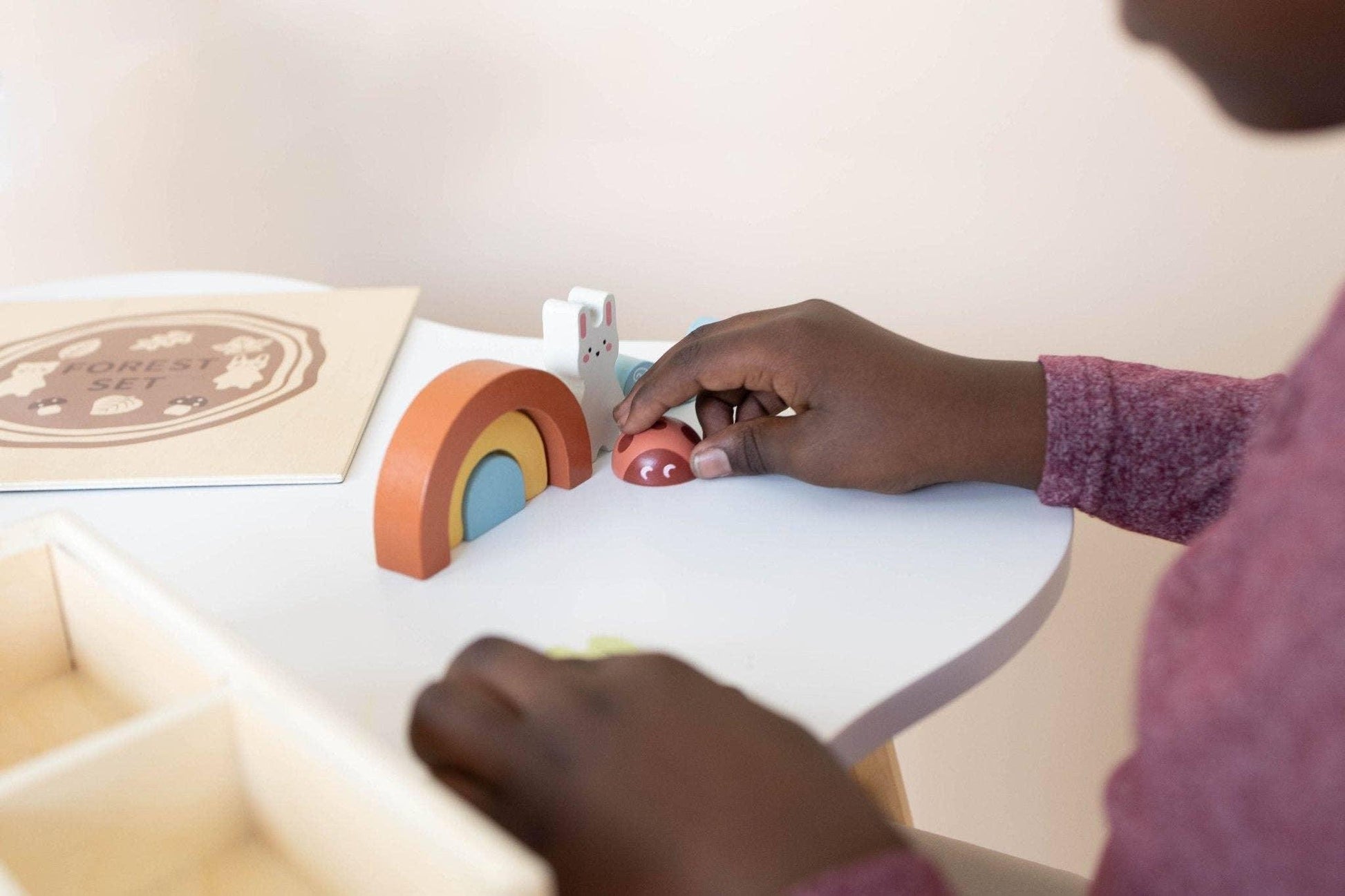 Child playing with wooden rainbow and animal toys on white table Come see us at Awaken, Franklin, Tennessee