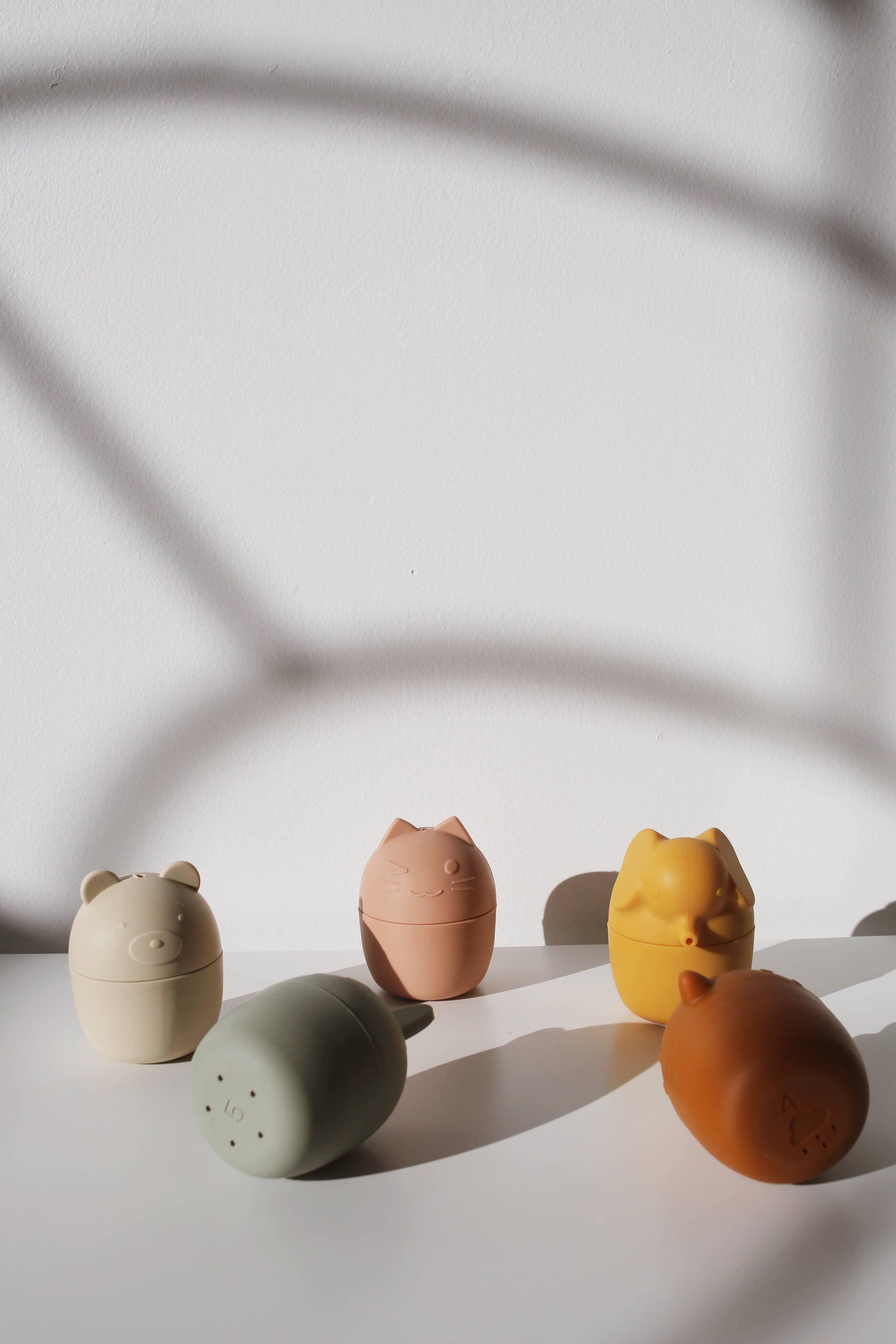 Colorful silicone animal-shaped containers on white surface with shadows. Come see us at Awaken, Franklin, Tennessee