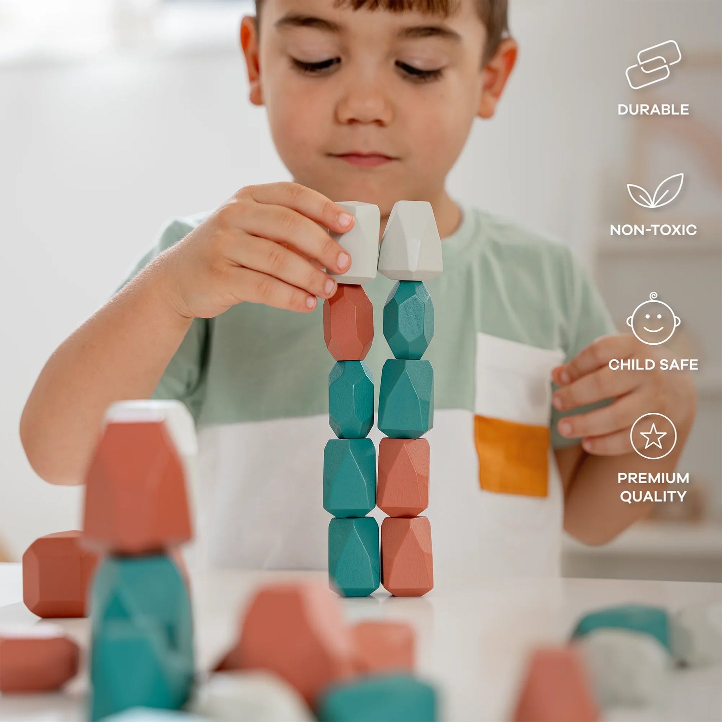 Young boy stacking colorful geometric wooden blocks on white table in bright room; child safe, non-toxic, durable toy. Come see us at Awaken, Franklin, Tennessee