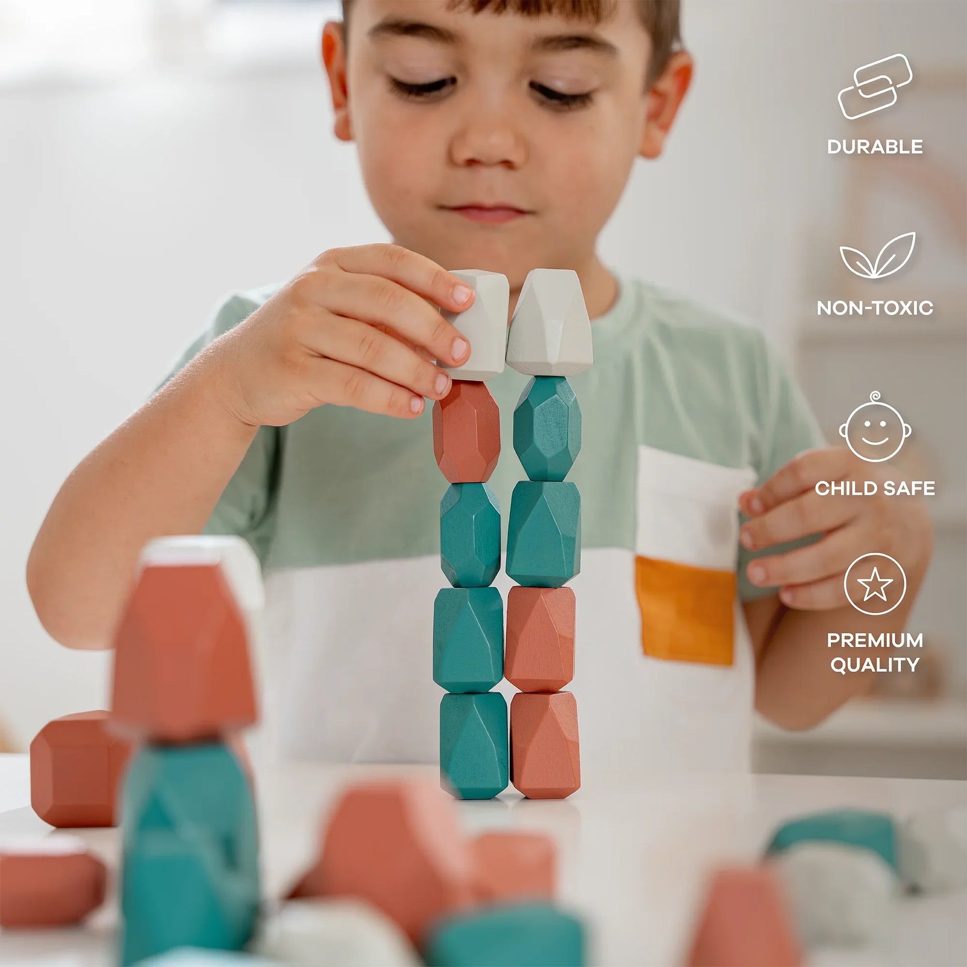 Young boy stacking colorful geometric wooden blocks on white table in bright room; child safe, non-toxic, durable toy. Come see us at Awaken, Franklin, Tennessee