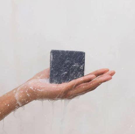 Hand holding a wet black soap bar with water dripping, minimal background. Come see us at Awaken, Franklin, Tennessee
