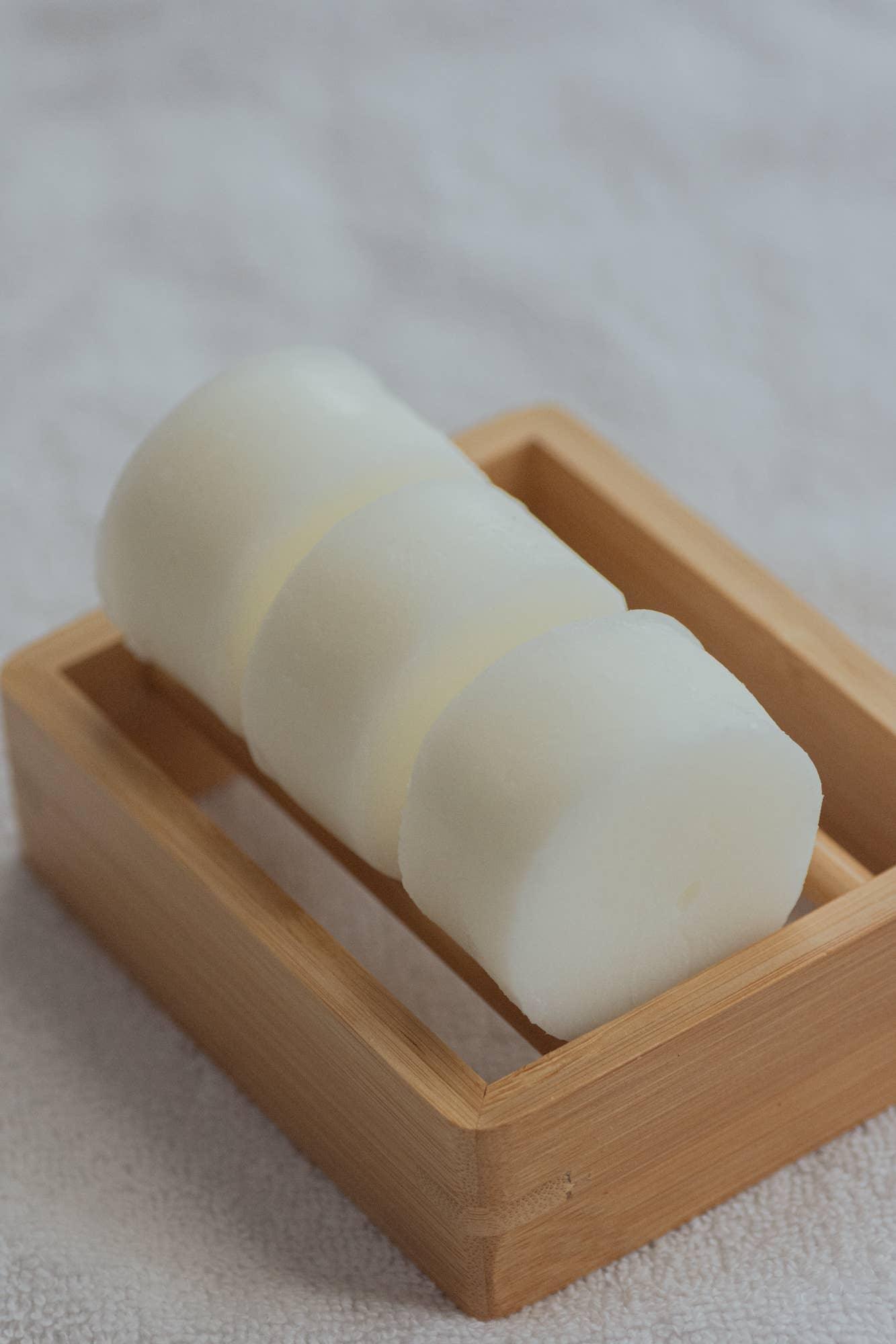 Three white soap bars in a wooden soap dish on a white textured towel. Come see us at Awaken, Franklin, Tennessee