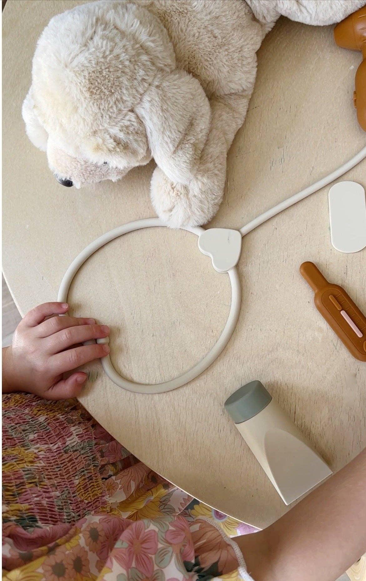 Child's hand playing with plush dog toy and toy medical kit on wooden table. Come see us at Awaken, Franklin, Tennessee