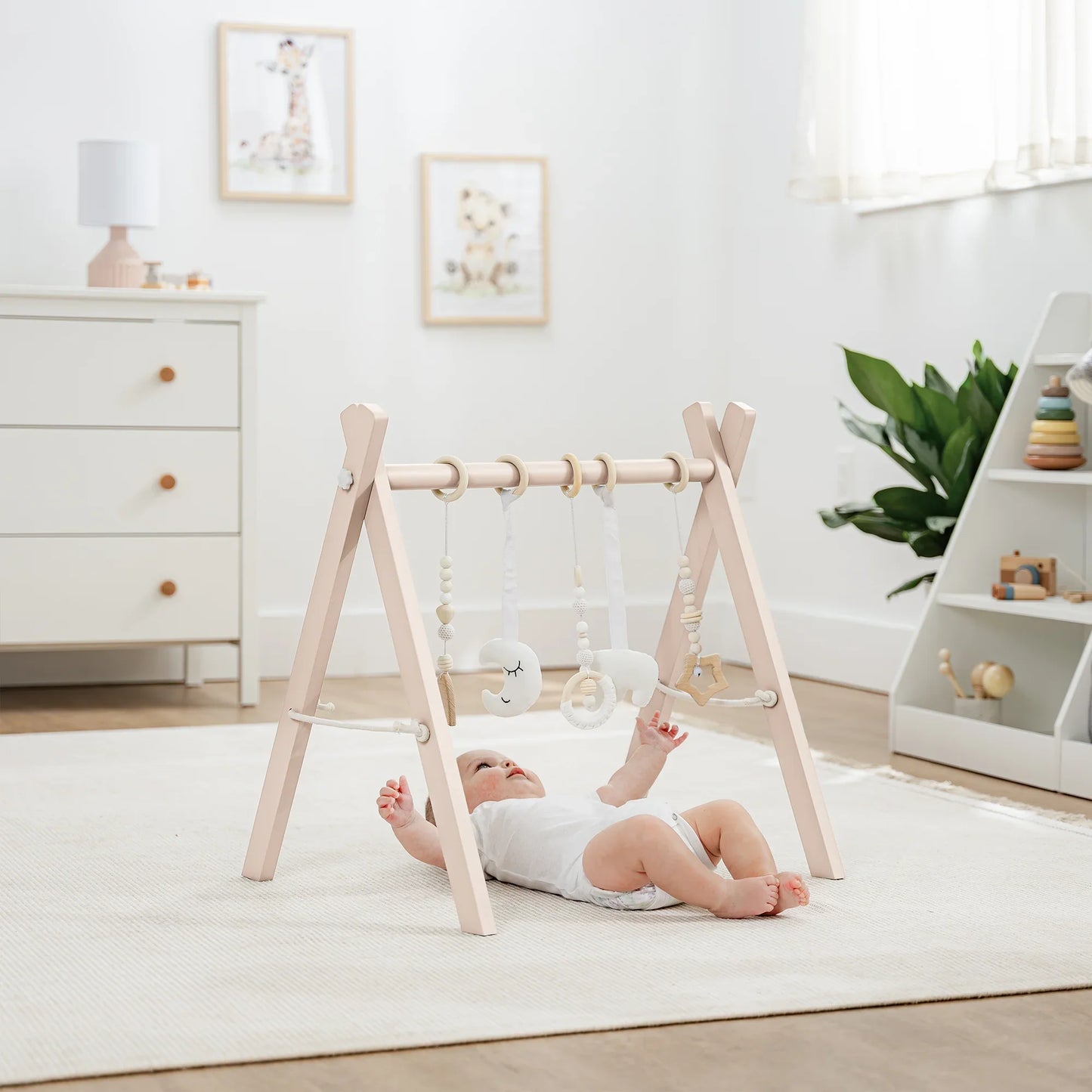 Baby lying under wooden play gym with hanging toys in bright nursery, Come see us at Awaken, Franklin, Tennessee