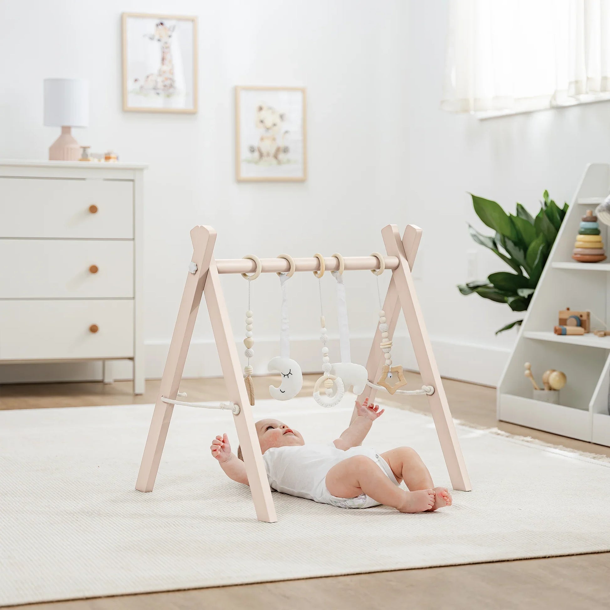 Baby lying under wooden play gym with hanging toys in bright nursery, Come see us at Awaken, Franklin, Tennessee