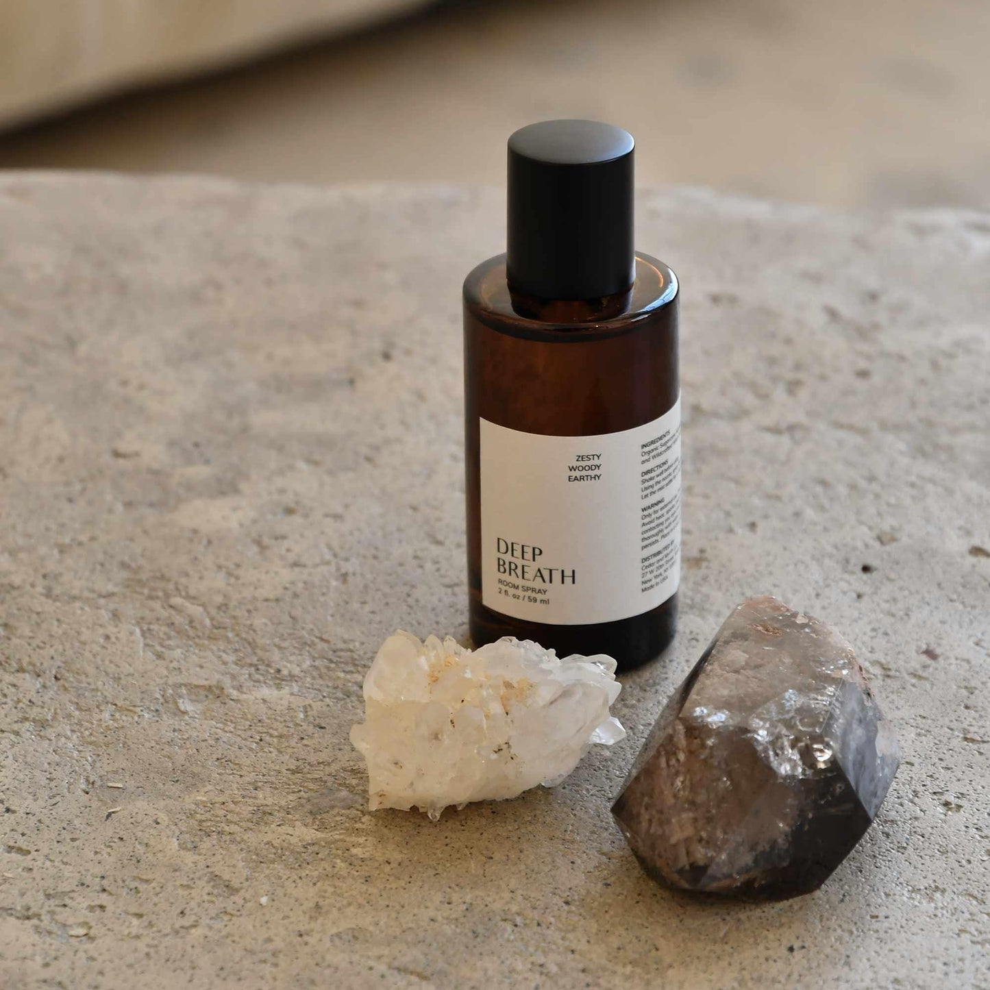 Deep Breath room spray bottle with crystal stones on textured surface, earth-toned setting. Come see us at Awaken, Franklin, Tennessee