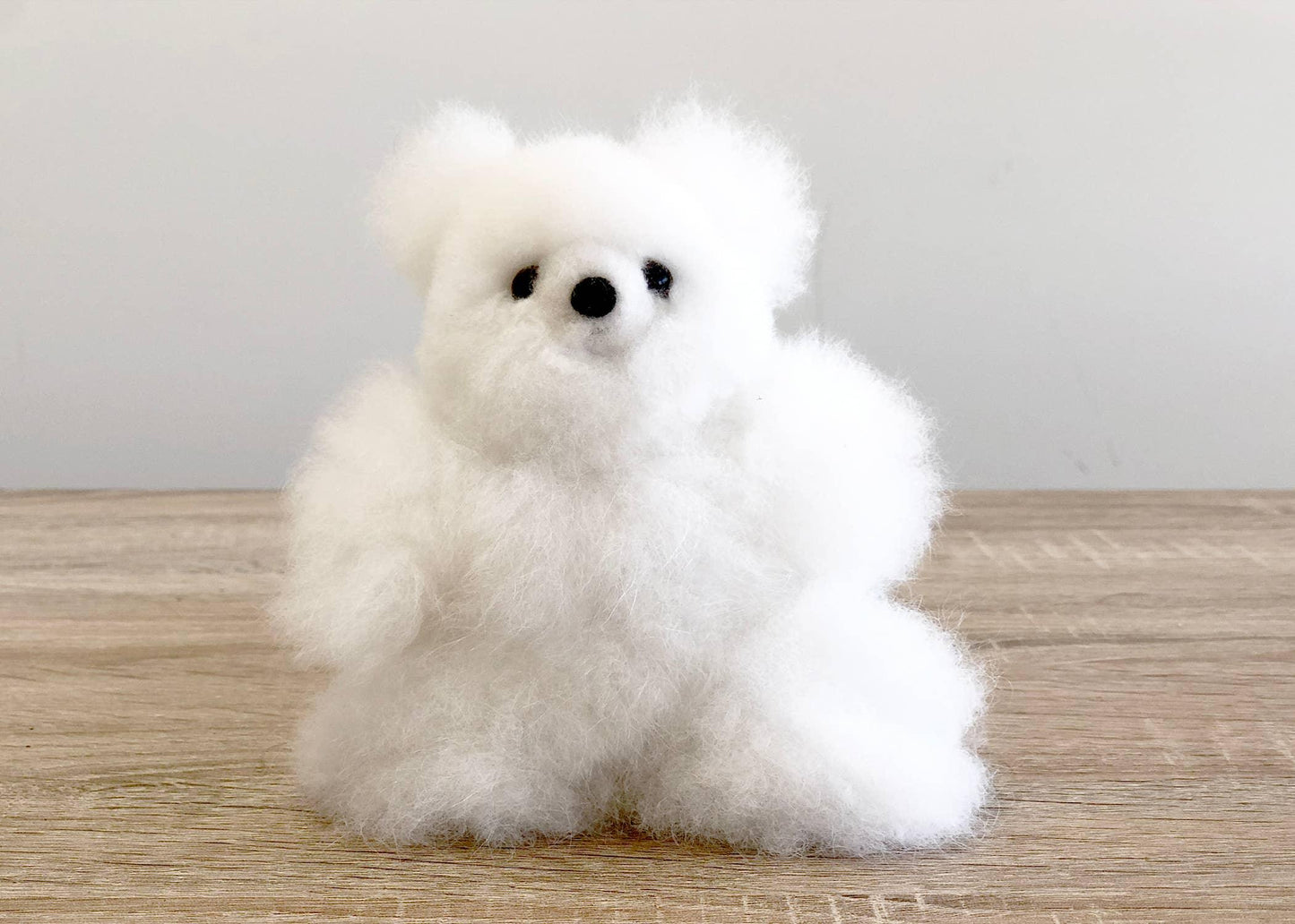 Fluffy white wool pomeranian dog figurine on wood surface, white background. Come see us at Awaken, Franklin, Tennessee