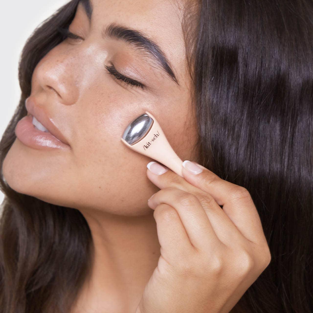 Woman using Kitsch facial massage tool on cheek with closed eyes, smooth skin, dark hair. Come see us at Awaken, Franklin, Tennessee