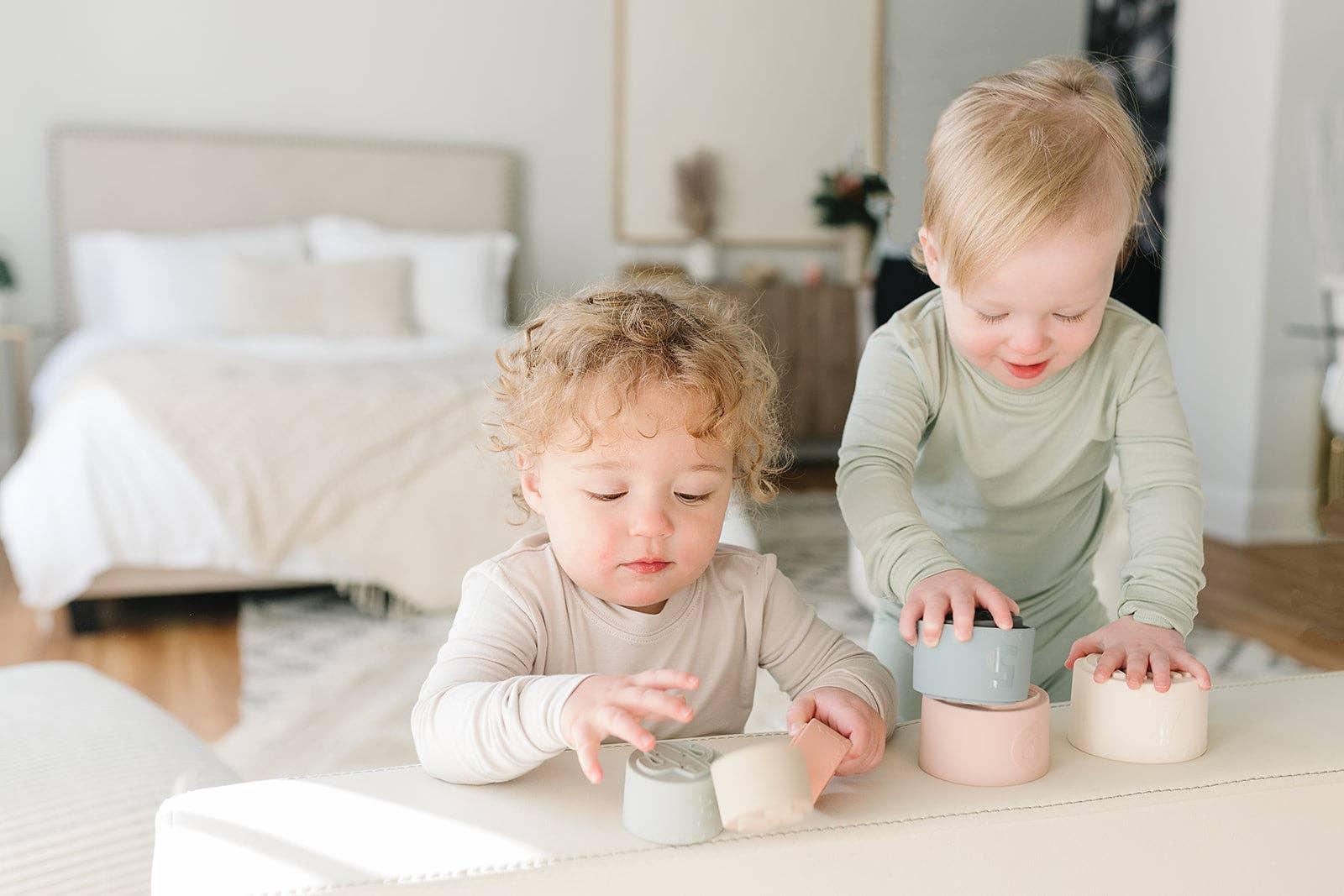 Two toddlers playing with pastel stacking cups in bright bedroom. Come see us at Awaken, Franklin, Tennessee