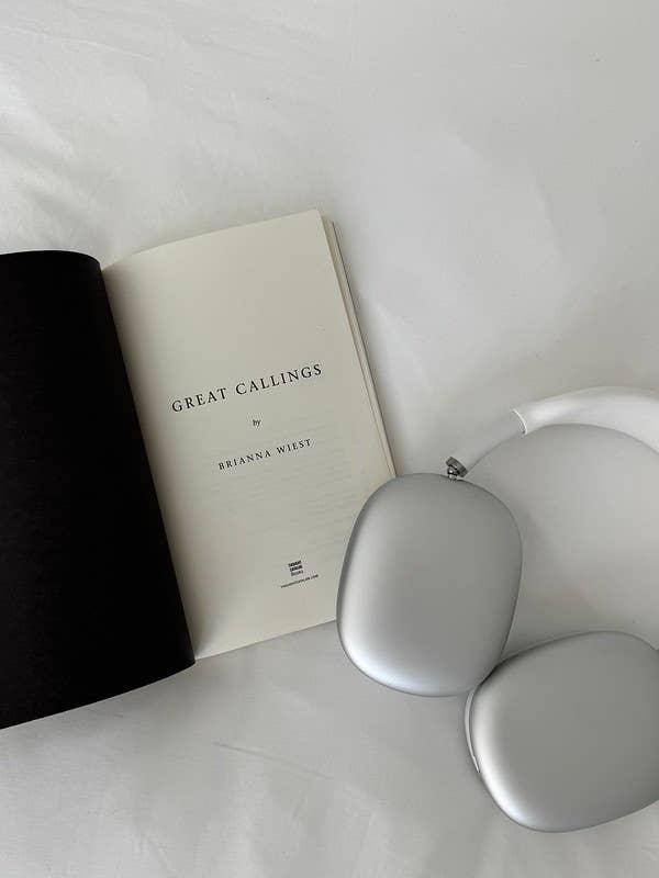 Open book titled Great Callings by Brianna Wiest beside silver wireless headphones Come see us at Awaken, Franklin, Tennessee