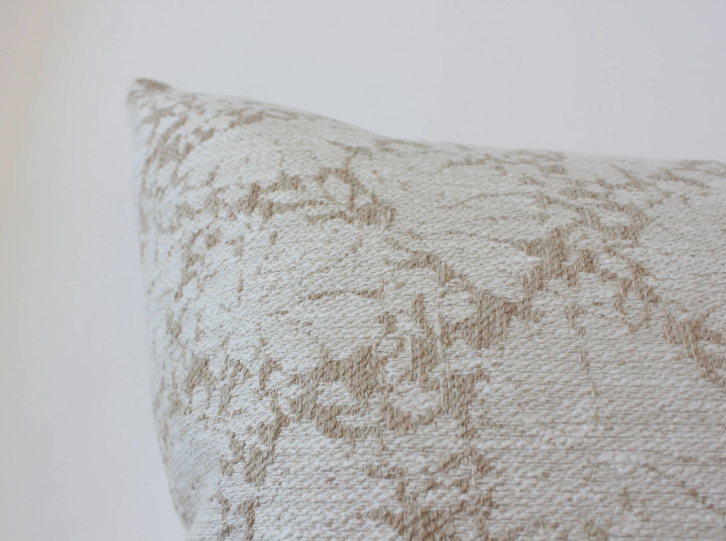 Close-up of beige textured decorative pillow with geometric pattern on white background. Come see us at Awaken, Franklin, Tennessee