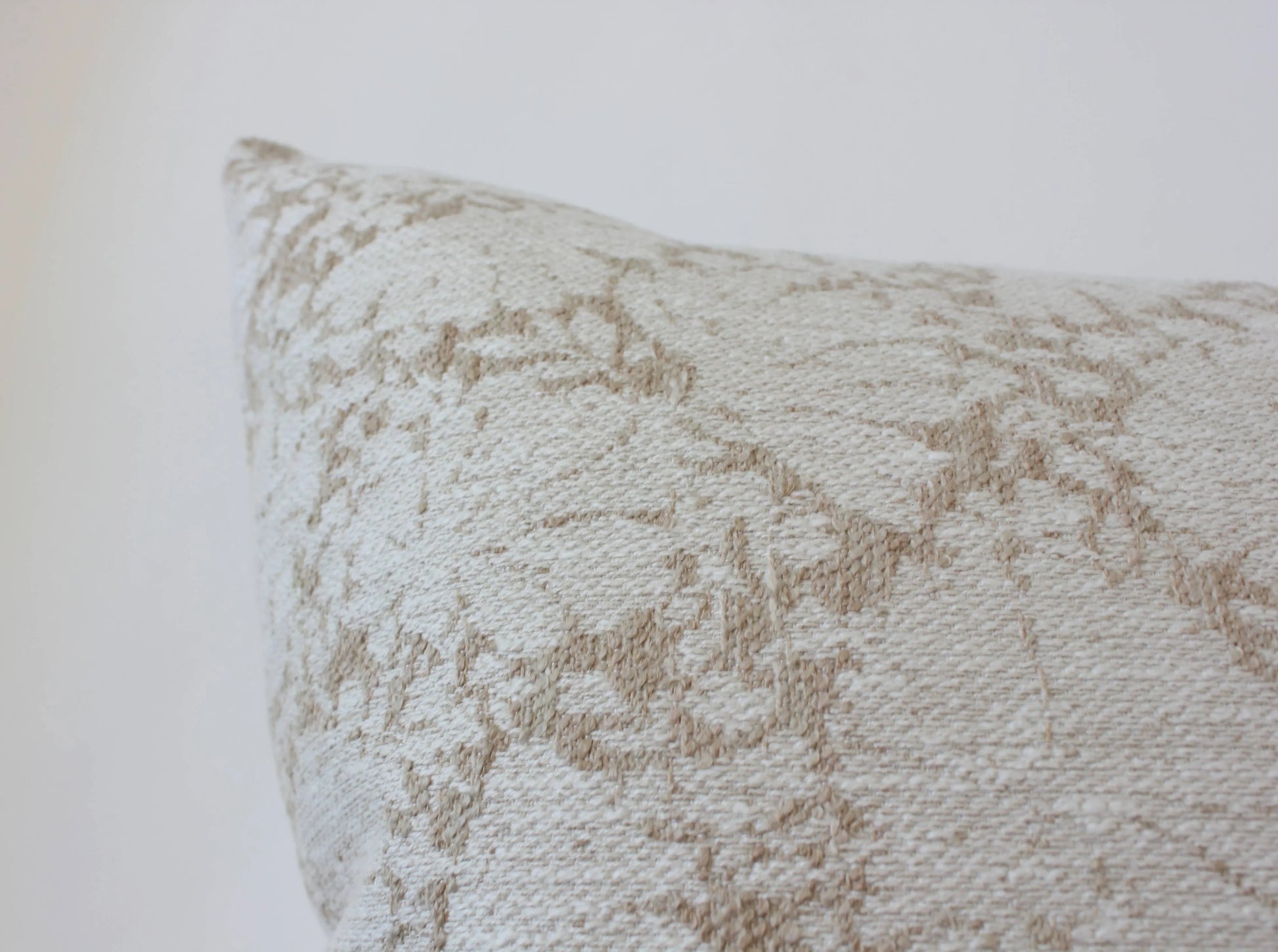 Close-up of beige textured decorative pillow with geometric pattern on white background. Come see us at Awaken, Franklin, Tennessee